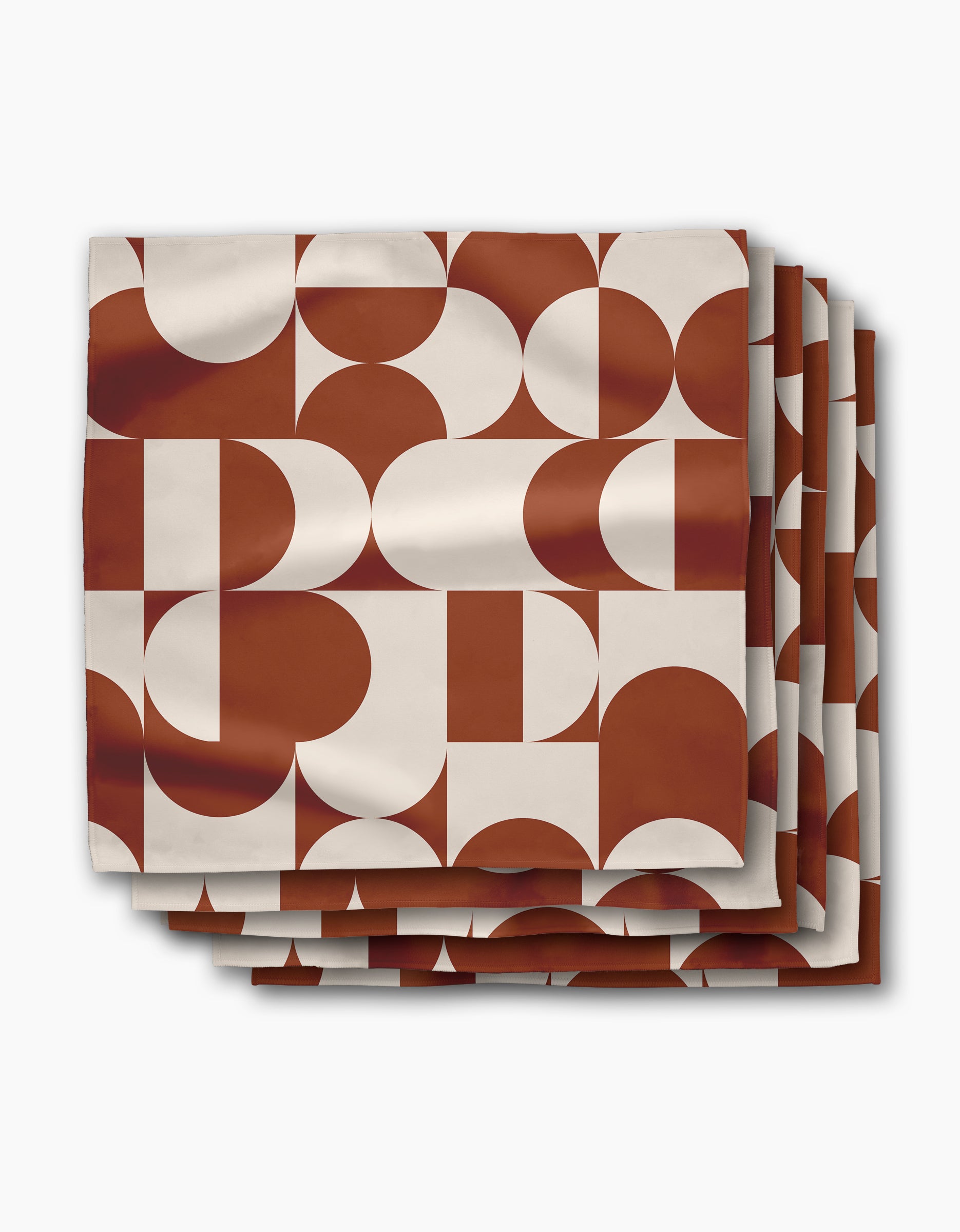 The Circle Playground dinner napkin set by Geometry includes four reusable cloth napkins, each featuring rust red and white geometric shapes on a crisp white background—perfect for adding style to any table setting.