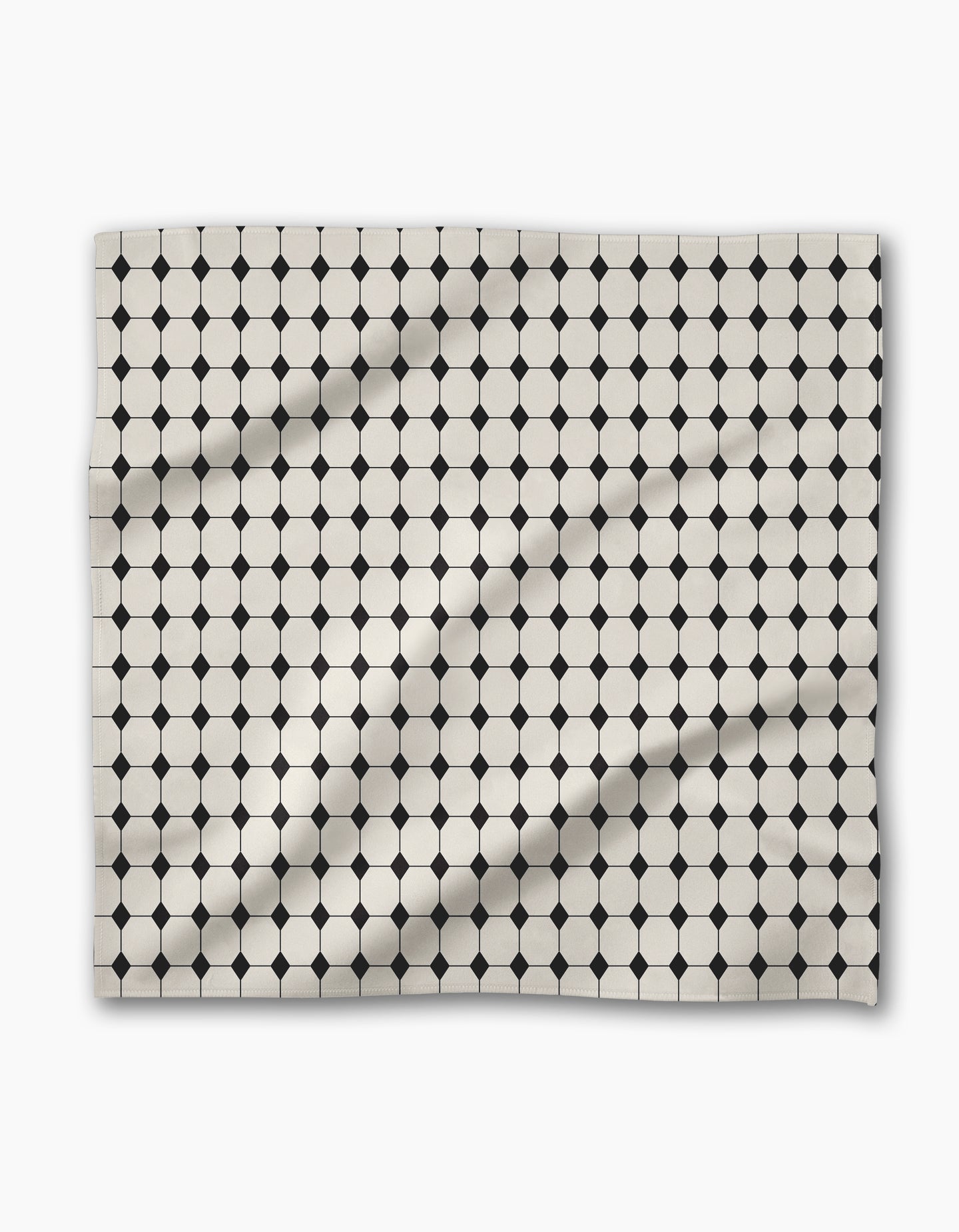 The Geometry Espresso Mosaic is a rectangular reusable napkin made from recycled materials, featuring a geometric pattern of white octagons and black squares, resembling tiled mosaic; subtle wrinkles may be present.
