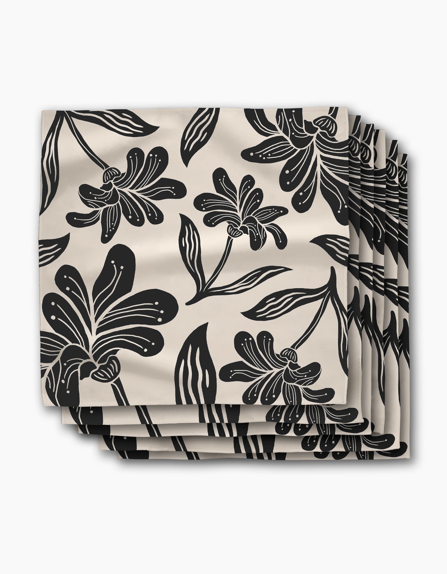 A set of four beige Geometry napkins in the Giant Lush Floral pattern, featuring bold black flowers and leaves, stacked and slightly fanned against a white background.