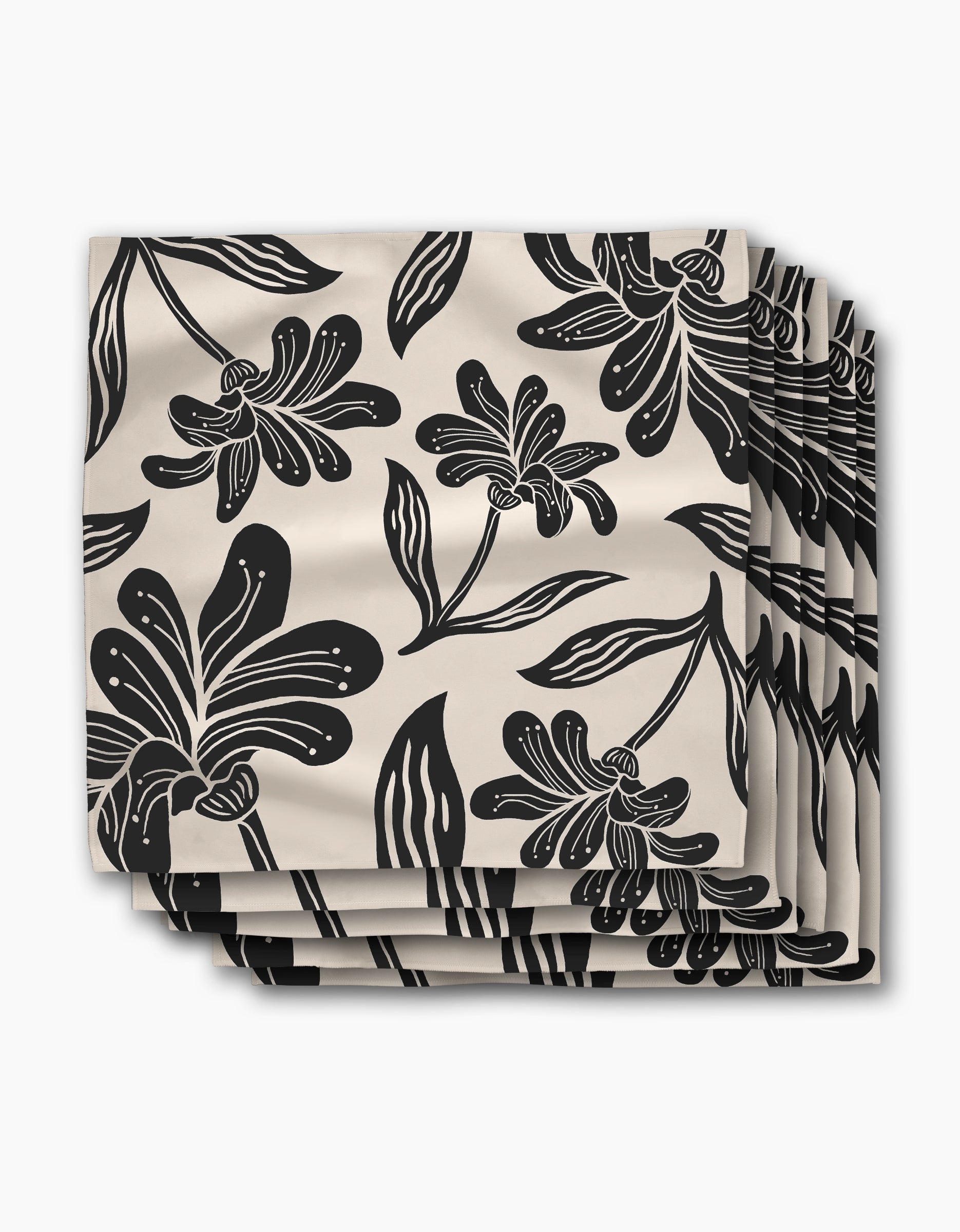 A set of four beige Geometry napkins in the Giant Lush Floral pattern, featuring bold black flowers and leaves, stacked and slightly fanned against a white background.