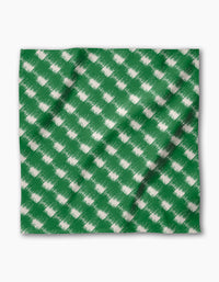 The Geometry Hairy Check Green is a reusable napkin made from recycled materials, featuring a green, square cloth with a white brushed, diagonal check pattern. It has slight folds and shadows, set against a plain white background.