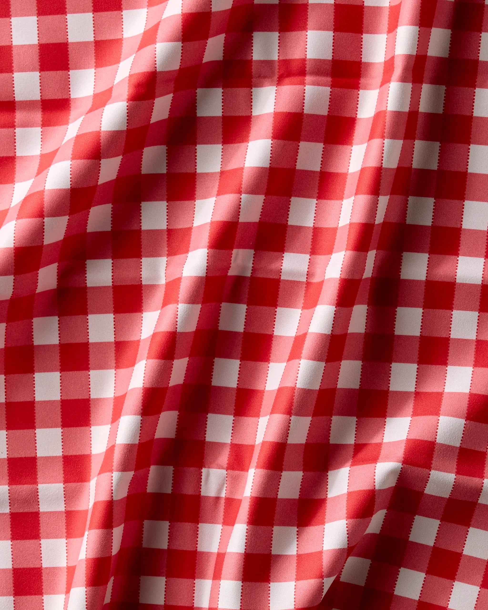 A close-up of Geometry's Ripe Tomato Gingham fabric shows red and white checkered folds, creating a textured look—resembling a classic picnic tablecloth, perfect for absorbent cloth napkins or a Dinner Napkin Set.
