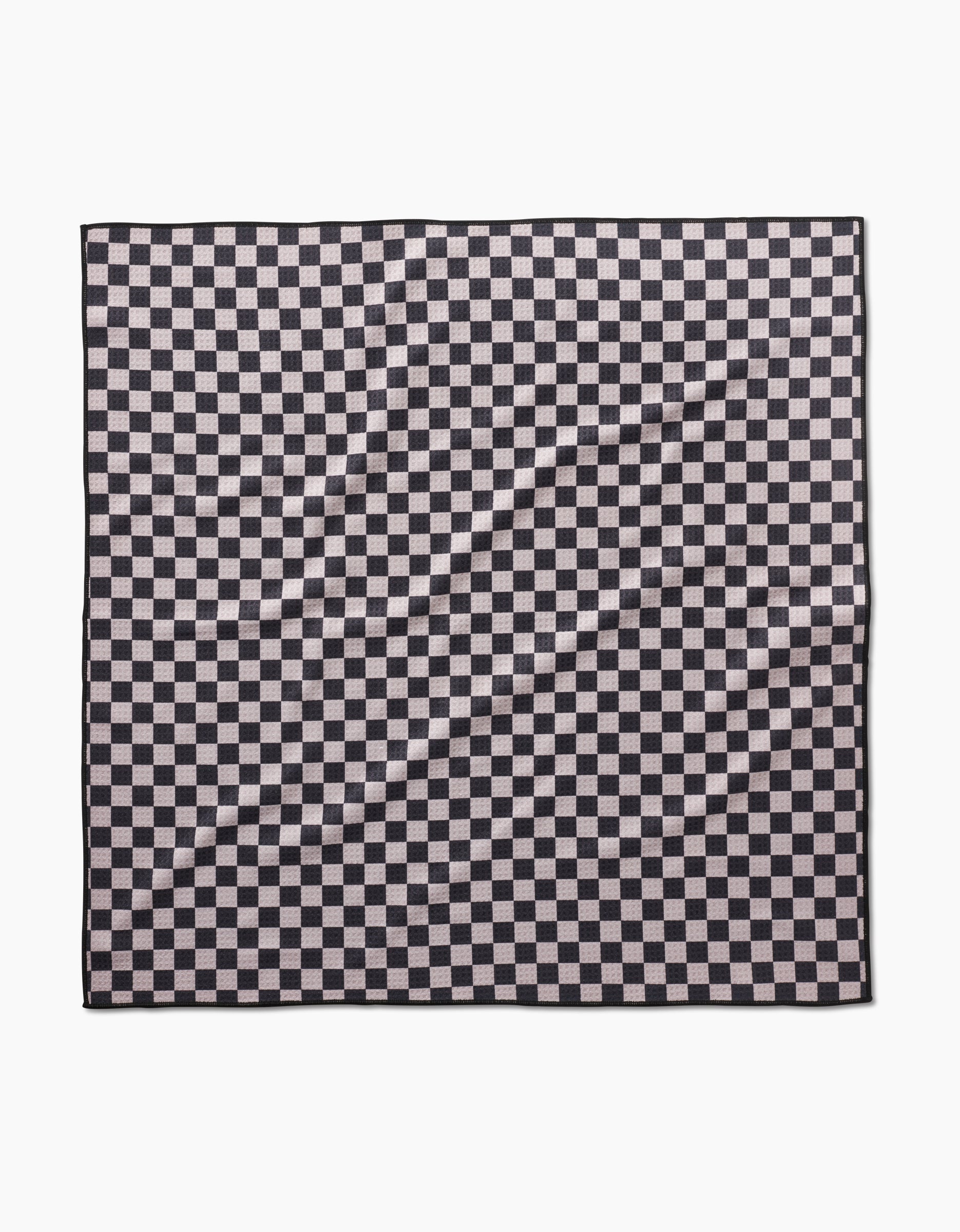 The Geometry Cool Pup dog towel in black and white checkered pattern lays flat, showing a wrinkled, highly absorbent surface with repeating squares.
