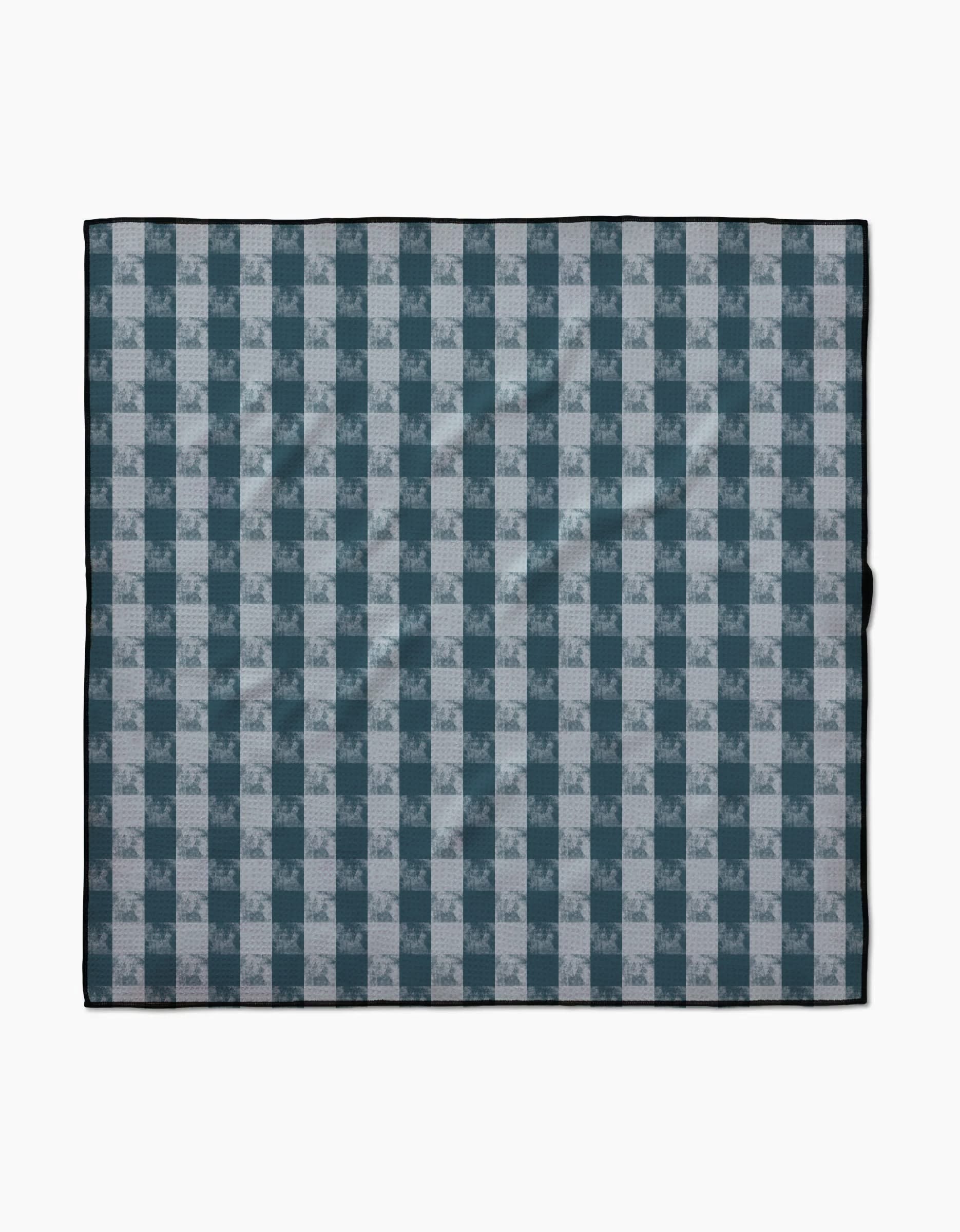 The Geometry Beach Storm blanket features a blue and white plaid pattern with alternating squares, a thin black border, and is made from recycled materials, shown laid flat on a white background.
