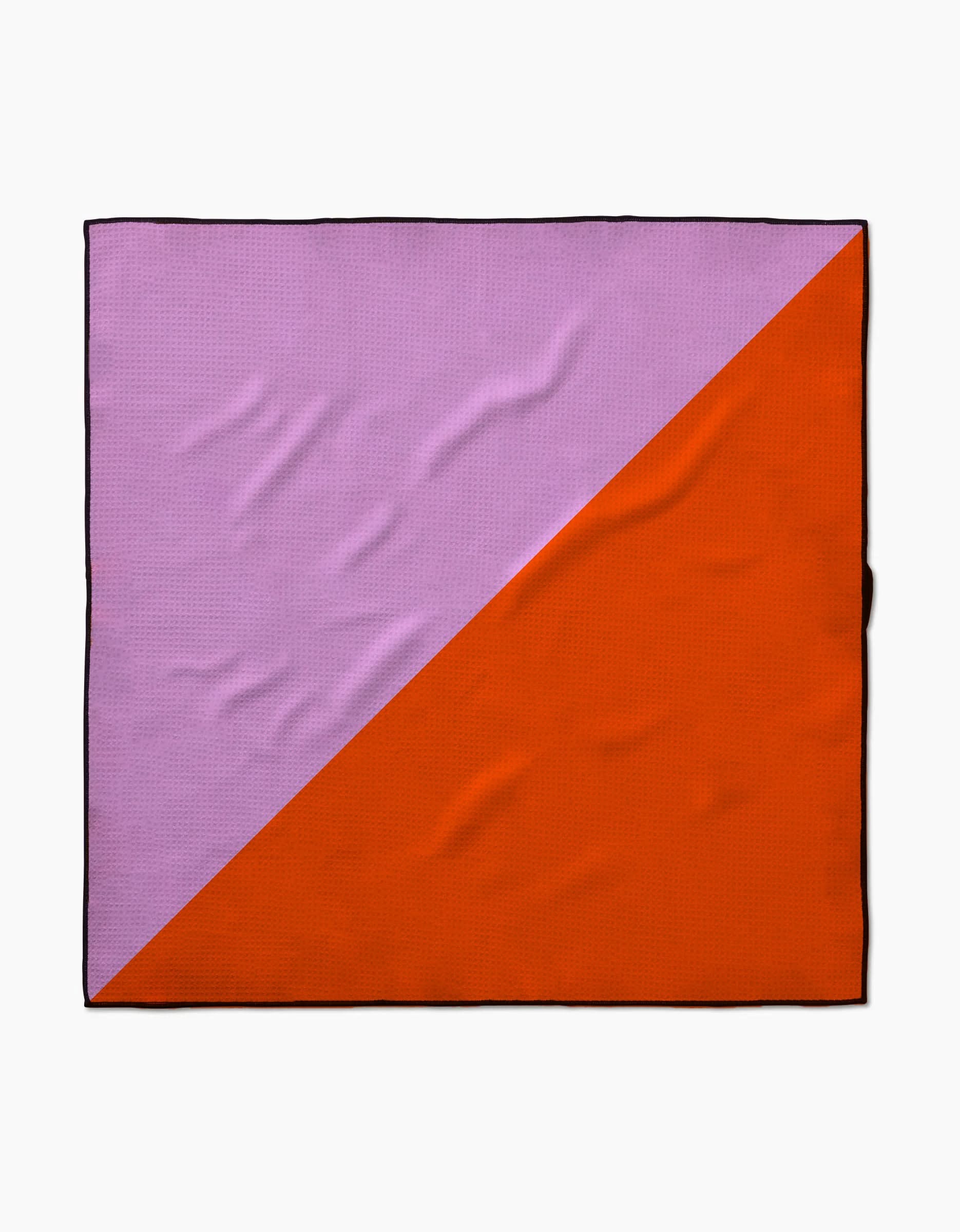 The Geometry Bold Horizon dog towel is square, made from recycled materials, with a diagonal split—light purple top left, orange bottom right—and a thin black border framing its highly absorbent fabric.