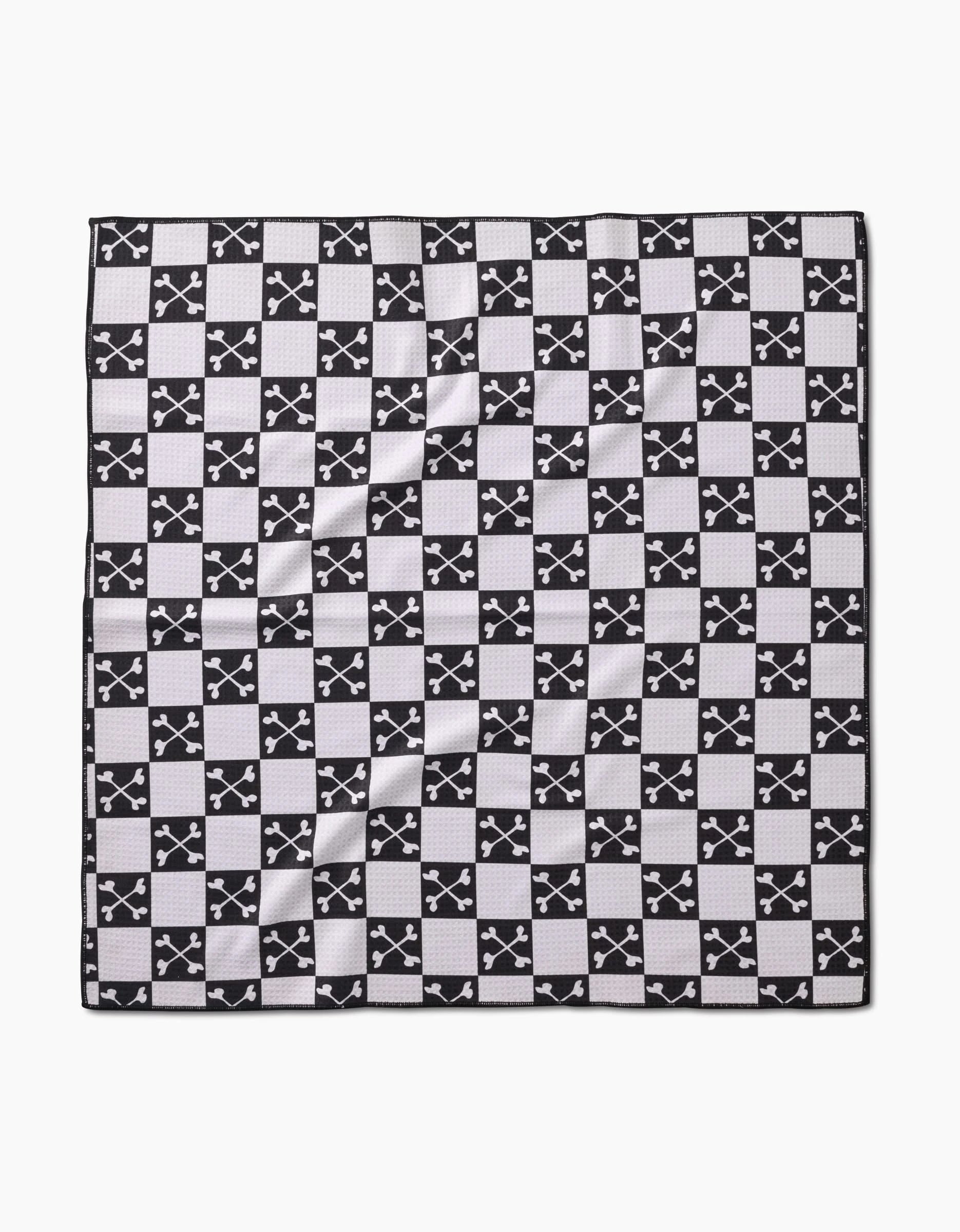 The Boneyard Black Checkerboard by Charlie Rowan Designs is a square dog towel made from recycled materials, featuring a black and white checkerboard pattern with crossed-swords emblems and a textured, eco-friendly feel.