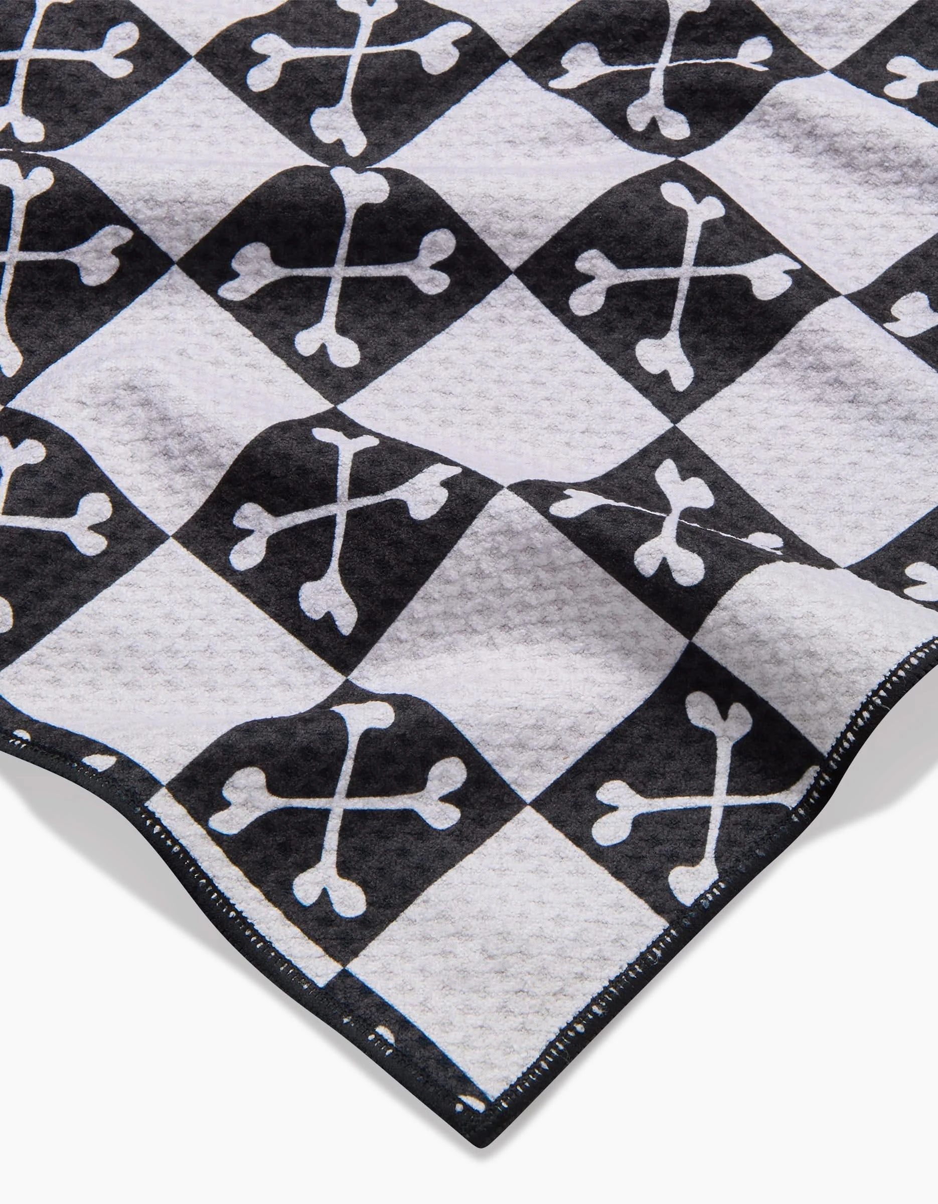 A close-up of the Boneyard Black Checkerboard dog towel by Charlie Rowan Designs, featuring crossed bones in each square, a textured and highly absorbent surface, and neatly stitched edges.
