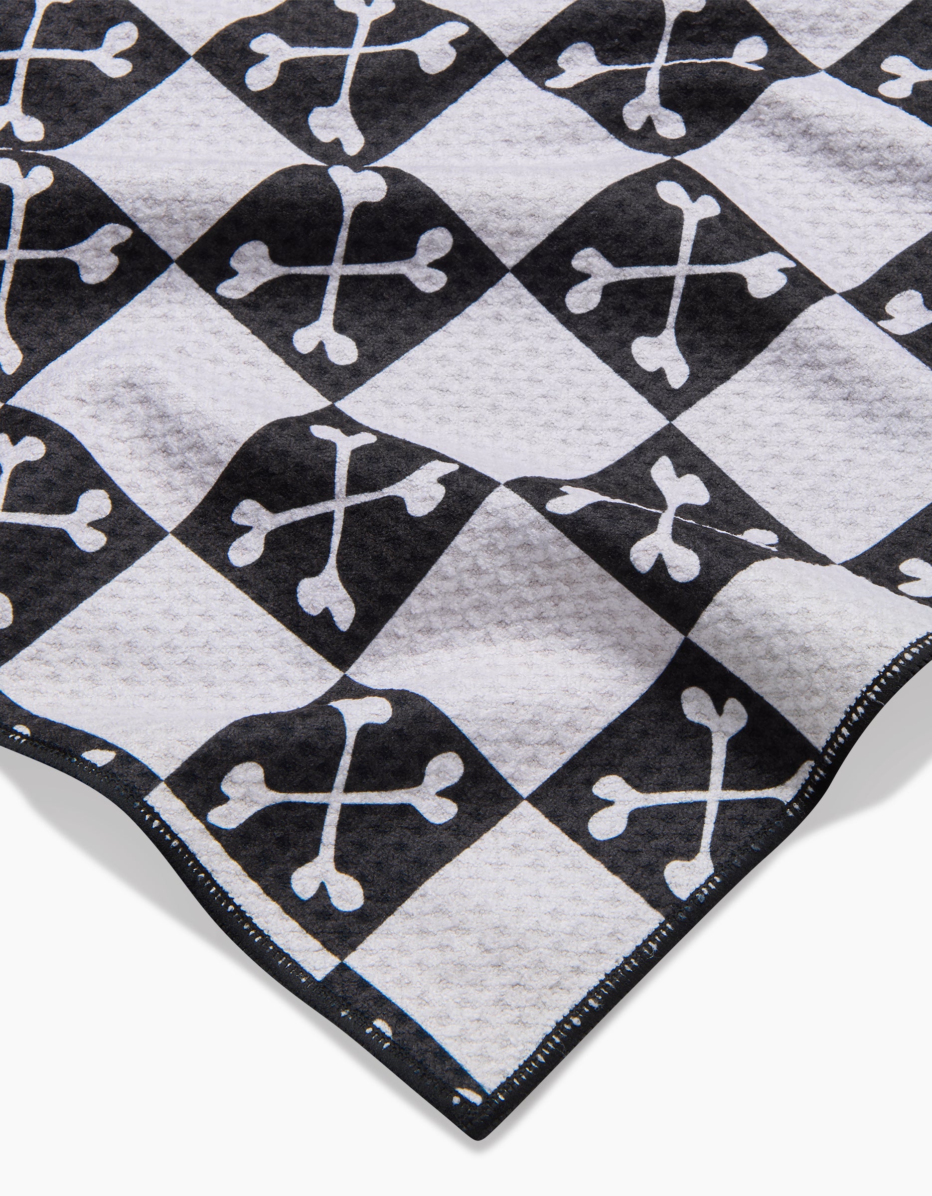 A close-up of the Boneyard Black Checkerboard dog towel by Charlie Rowan Designs, featuring crossed bones in each square, a textured and highly absorbent surface, and neatly stitched edges.