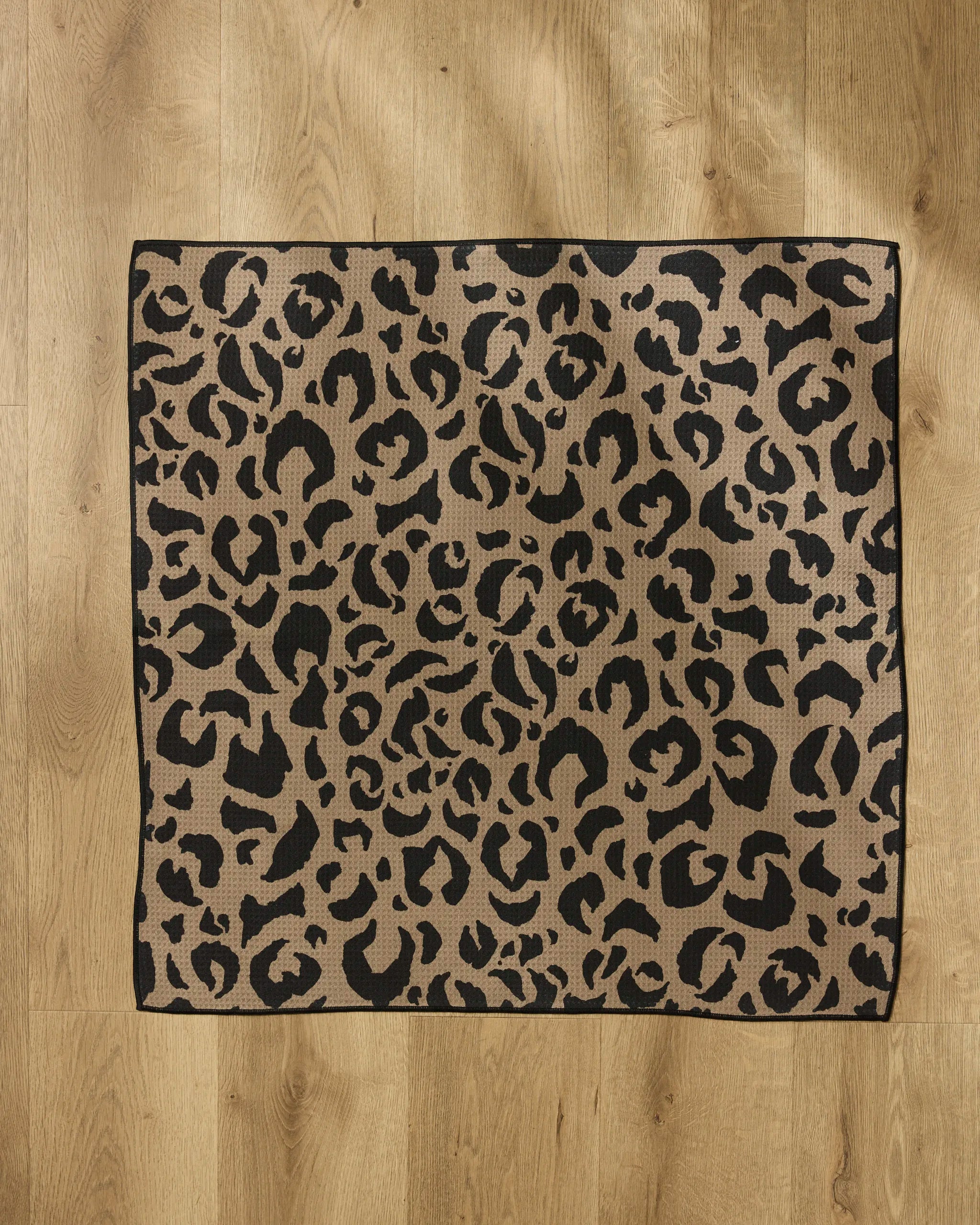The Cheetah Hound rug by Geometry is square, crafted from recycled materials, and features a beige base with striking black leopard spots—perfect for enhancing light wooden floors.
