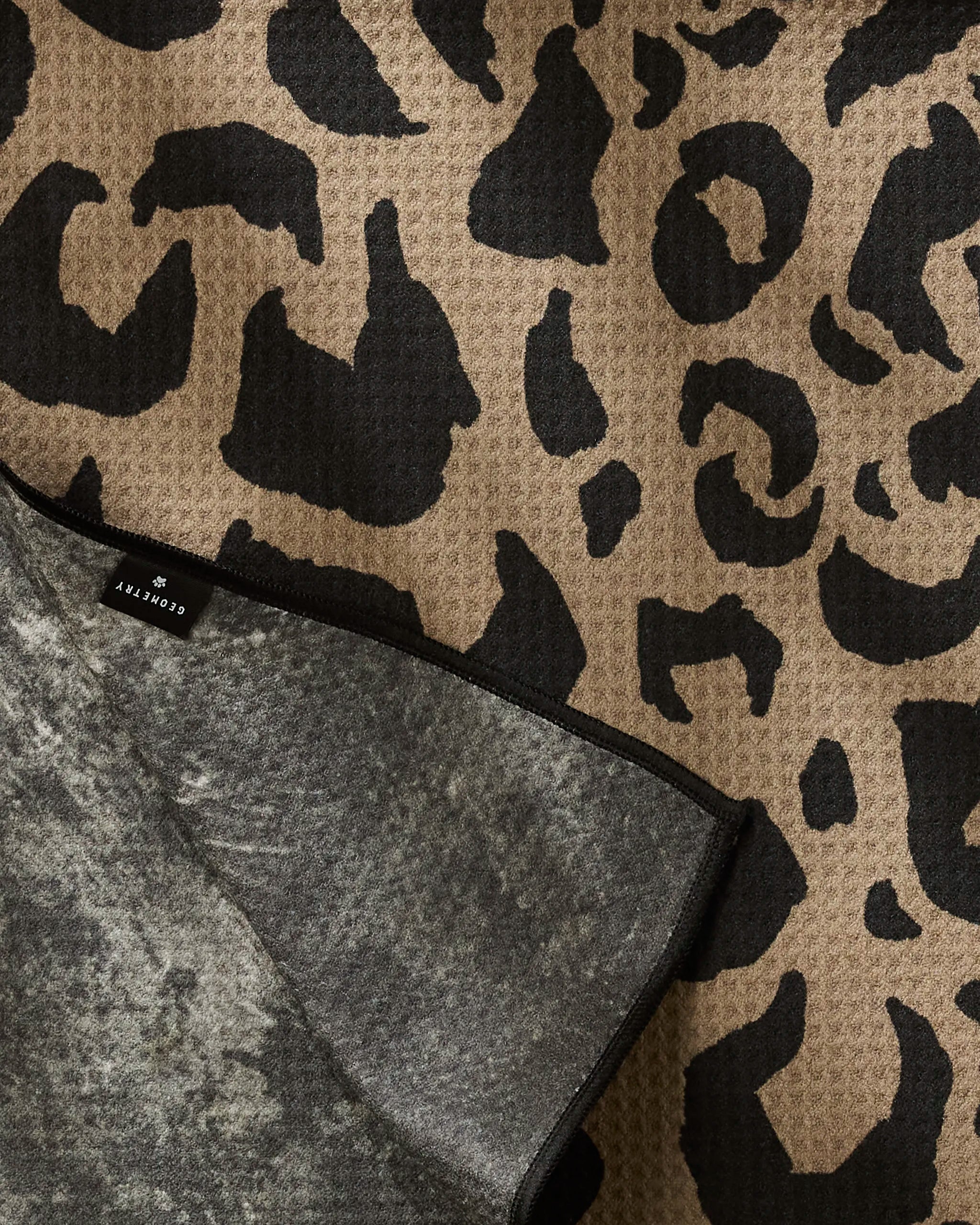 A close-up of Geometry's Cheetah Hound fabric—made from recycled materials—with a brown and black leopard print, partially folded to show the underside and a small black “CONVERTLY” tag.