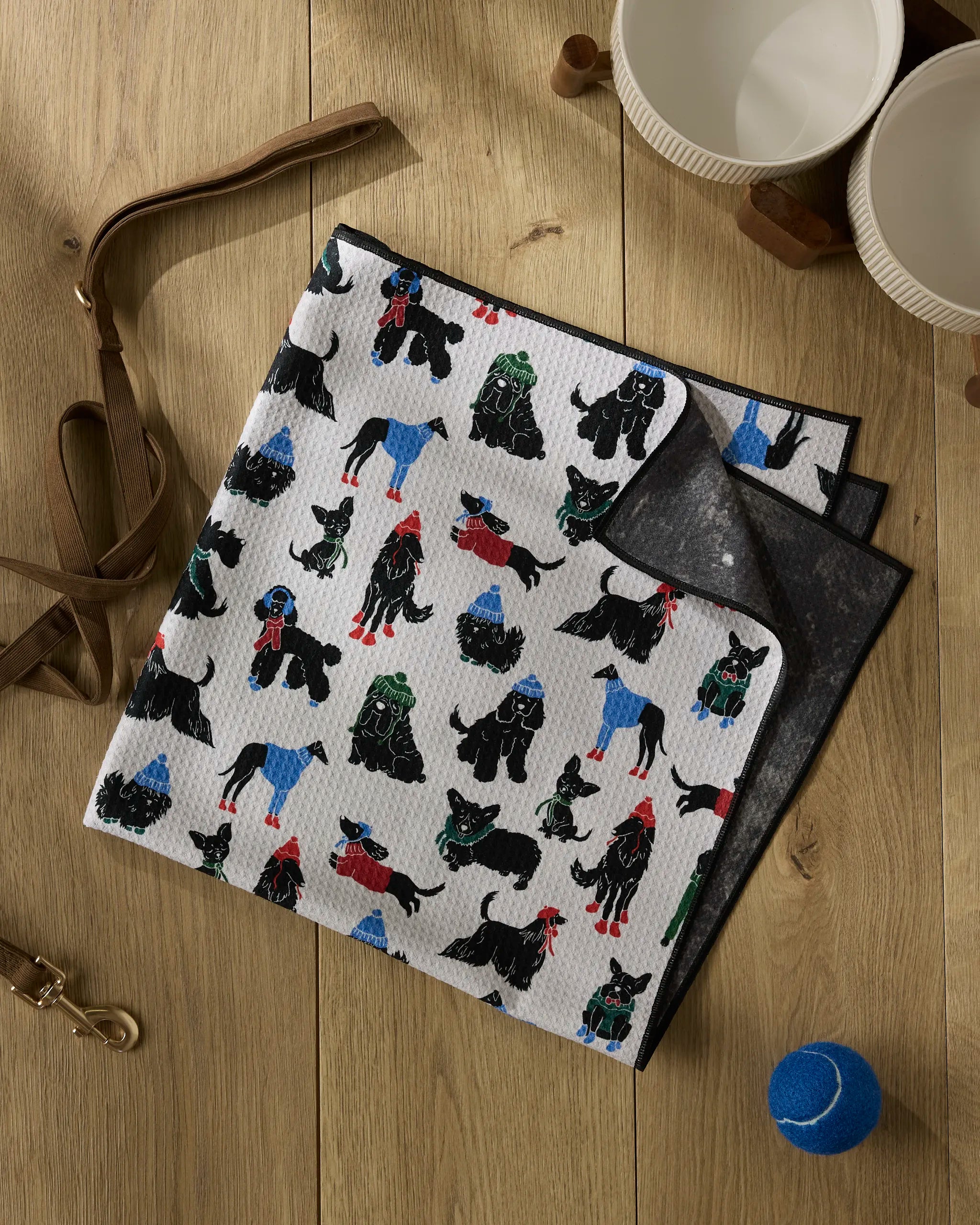 The Dogue Magazine by Geometry lies folded on a wooden surface beside two empty bowls, an apron, a collar, and a blue tennis ball. Its cover features adorable dogs in colorful sweaters.