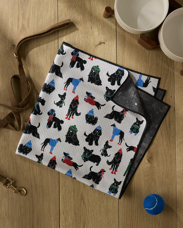 The Dogue Magazine by Geometry lies folded on a wooden surface beside two empty bowls, an apron, a collar, and a blue tennis ball. Its cover features adorable dogs in colorful sweaters.
