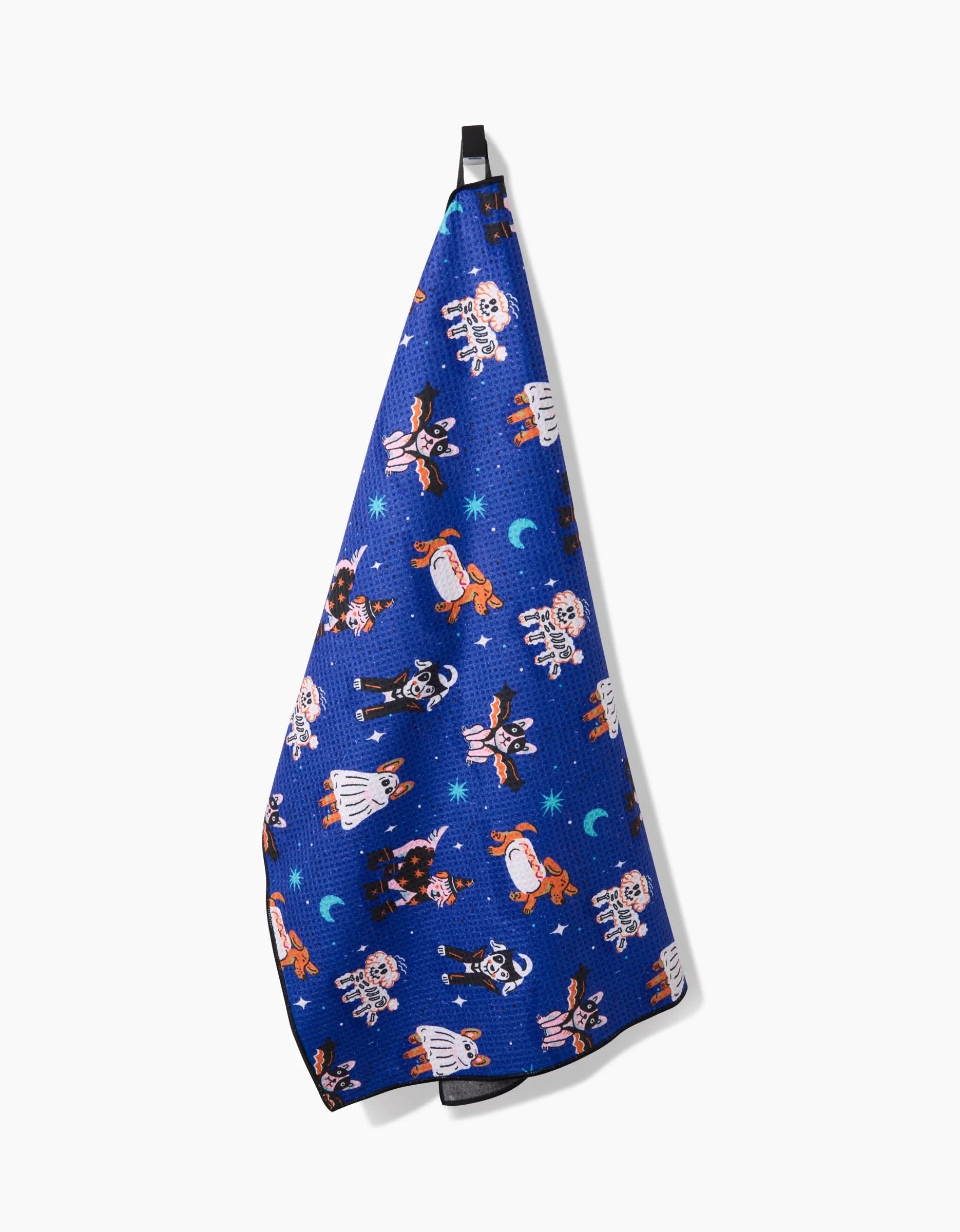 The Halloween Hounds towel by Camila Leão is blue, made from recycled materials, and features cartoon dogs dressed as astronauts with stars and moons, hanging from a black loop against a white background.