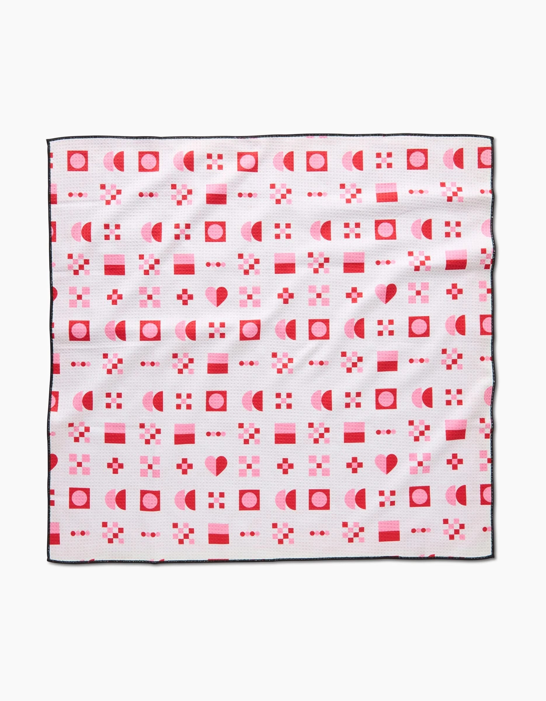 The Laura Supnik Heart Quilt is a square absorbent dog towel with a white background, black edges, and a grid pattern of red and pink hearts, squares, circles, and geometric shapes.