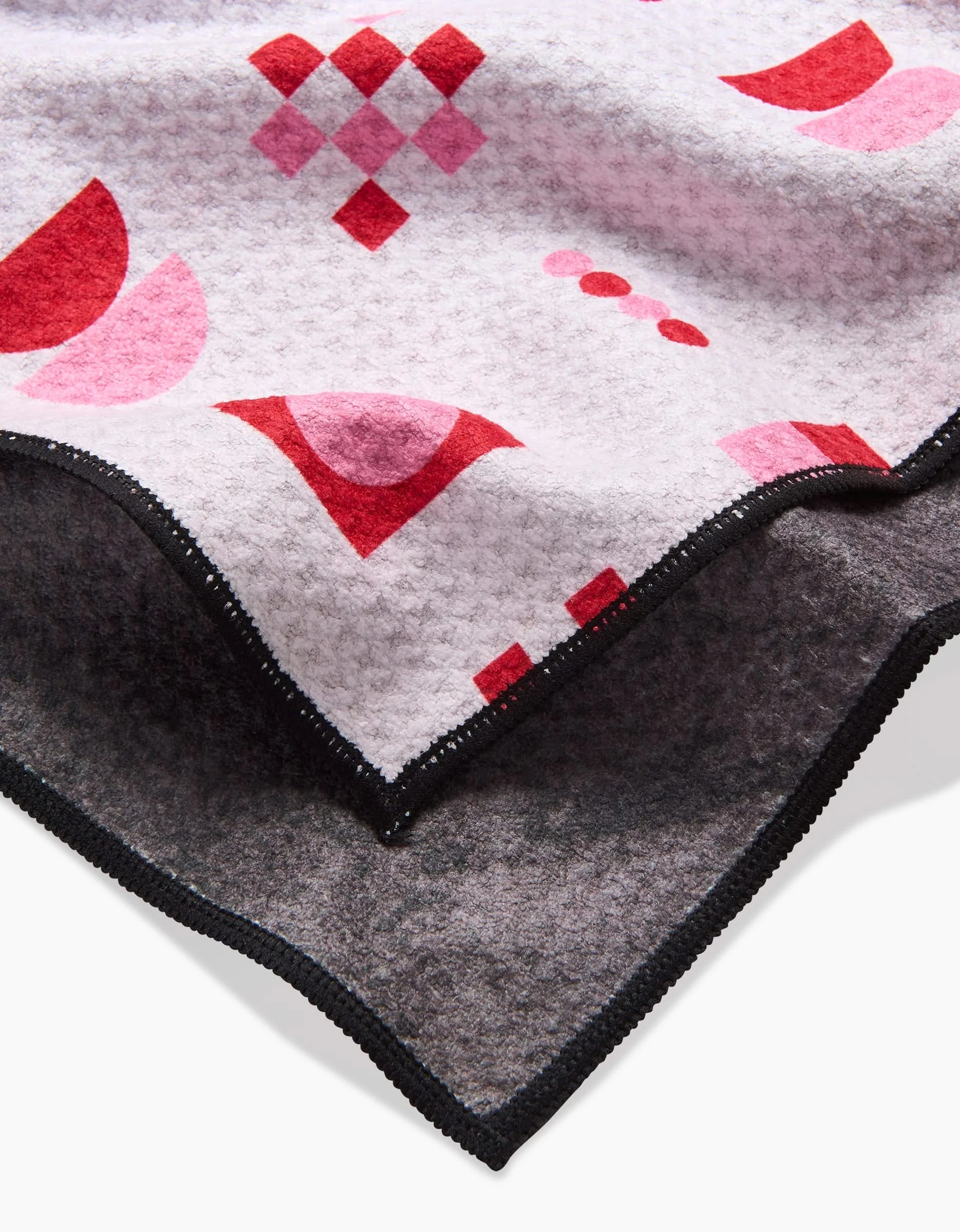 A close-up of the Laura Supnik Heart Quilt, a soft recycled dog towel with a white and pink surface featuring geometric red and pink shapes, plus a dark gray underside with black stitched edges.