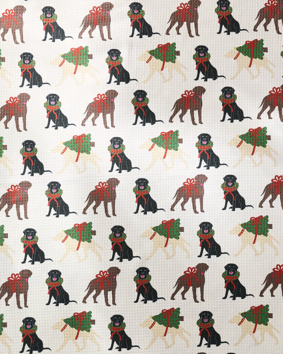 Merry Labs by Geometry features rows of cartoon dogs—black and brown Labradors sporting red scarves and bows, alongside pale pups carrying green wreaths with red bows—all set against a white textured background. Inspired by the classic dog towel, this patterned paper is printed on highly absorbent, recycled materials.