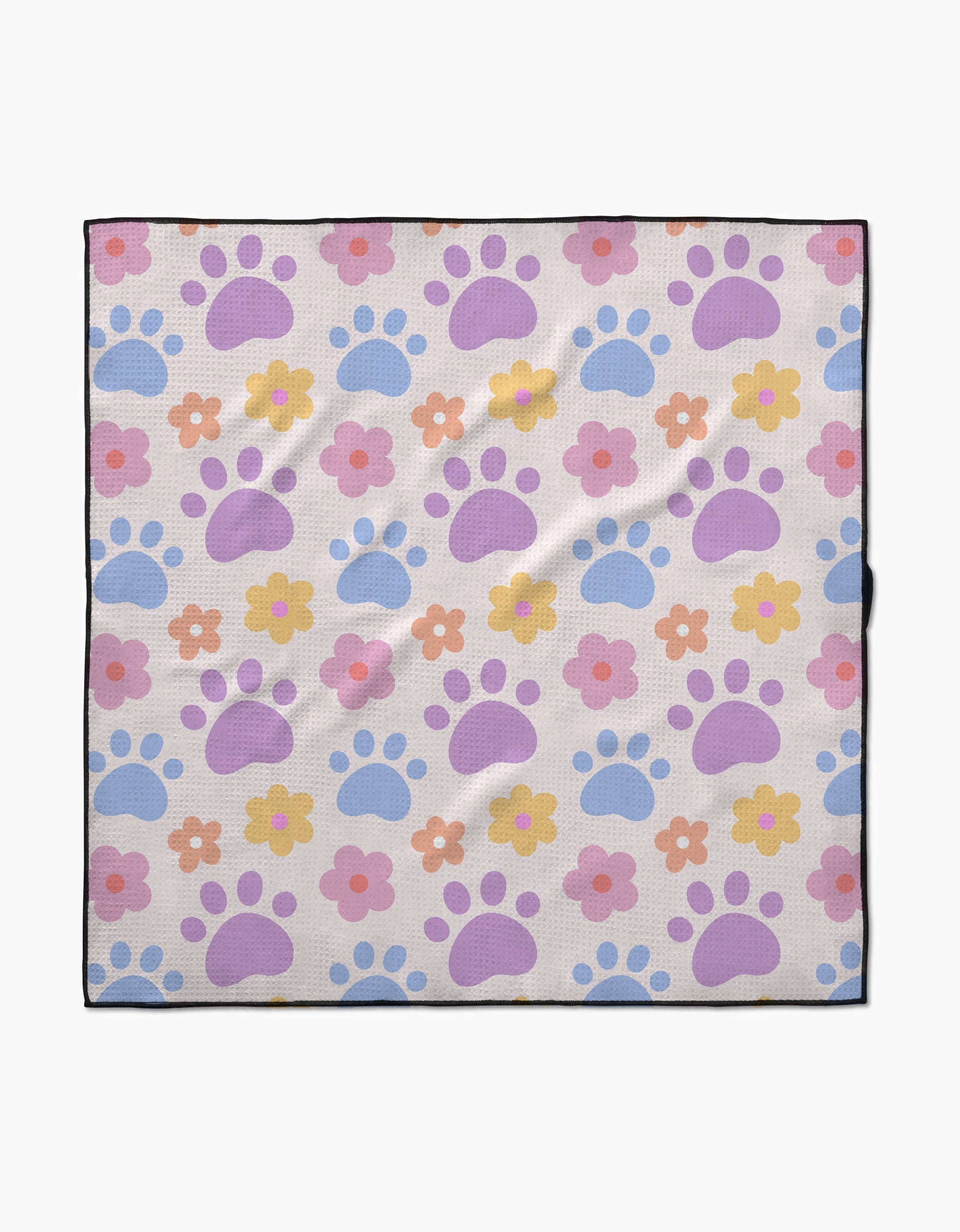 The Paws and Daisies dog towel by Letters By Shells is highly absorbent, made from recycled materials, and features pastel blue and purple paw prints with pink, orange, and yellow flowers on a light background with a slim black border.