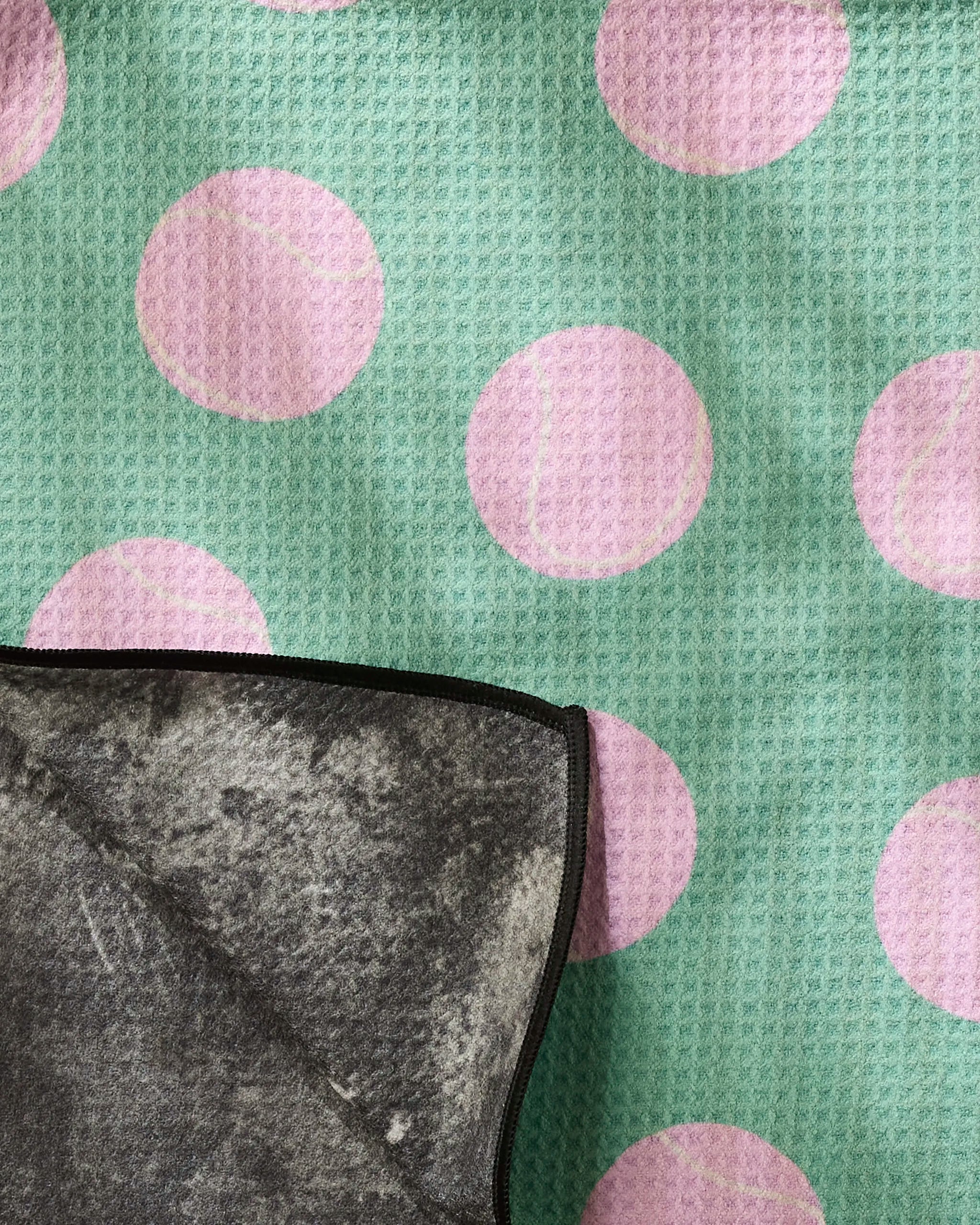 A textured green Pink Ball fabric by Geometry, featuring large pink tennis balls, is shown with a partially folded, highly absorbent gray Dog towel with black edging in the bottom left corner.