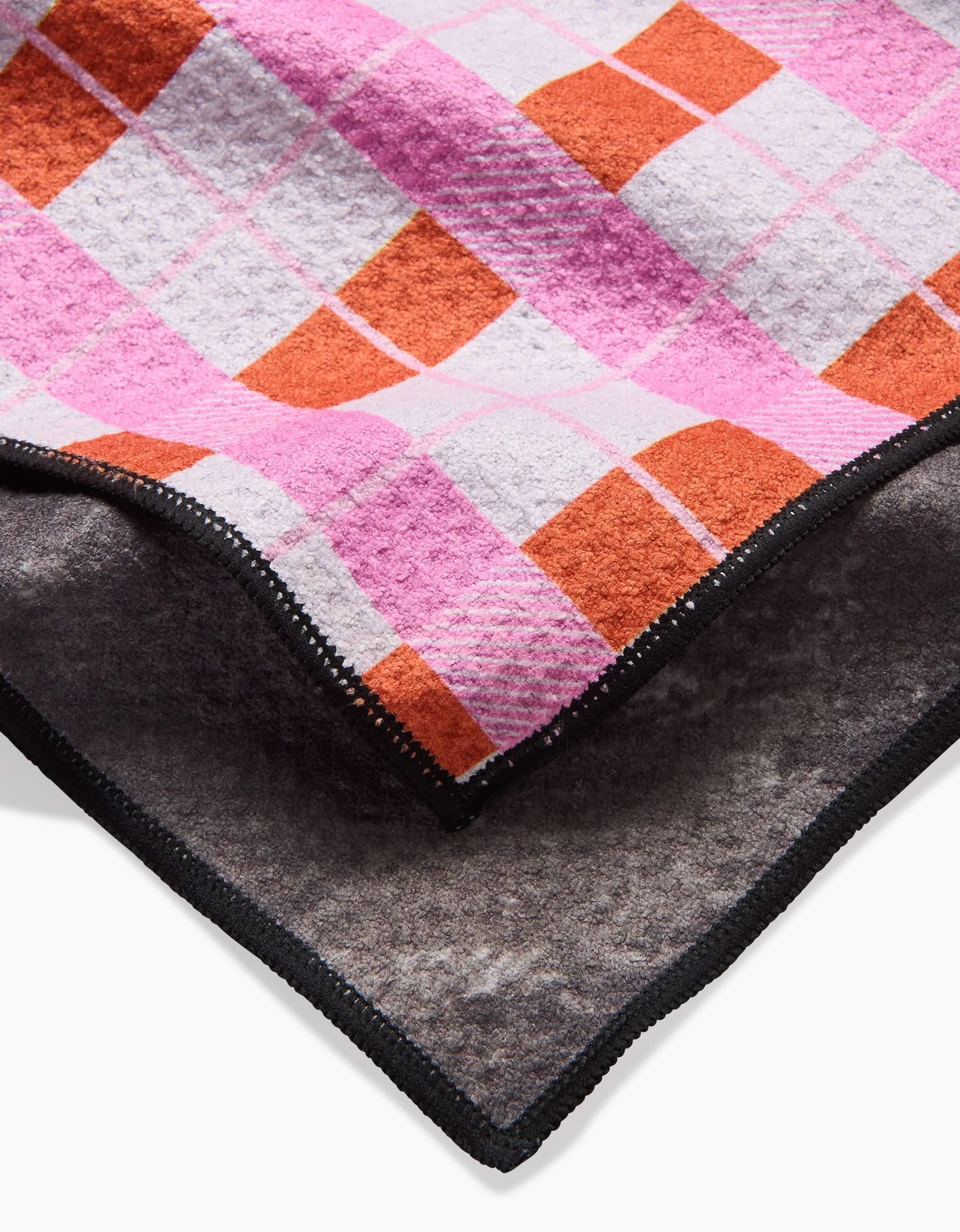 A close-up of the Megan Roy Red Pink Plaid dog towel, made from recycled materials with a pink, white, and orange checkered side, soft dark gray reverse, and black-stitched edges.