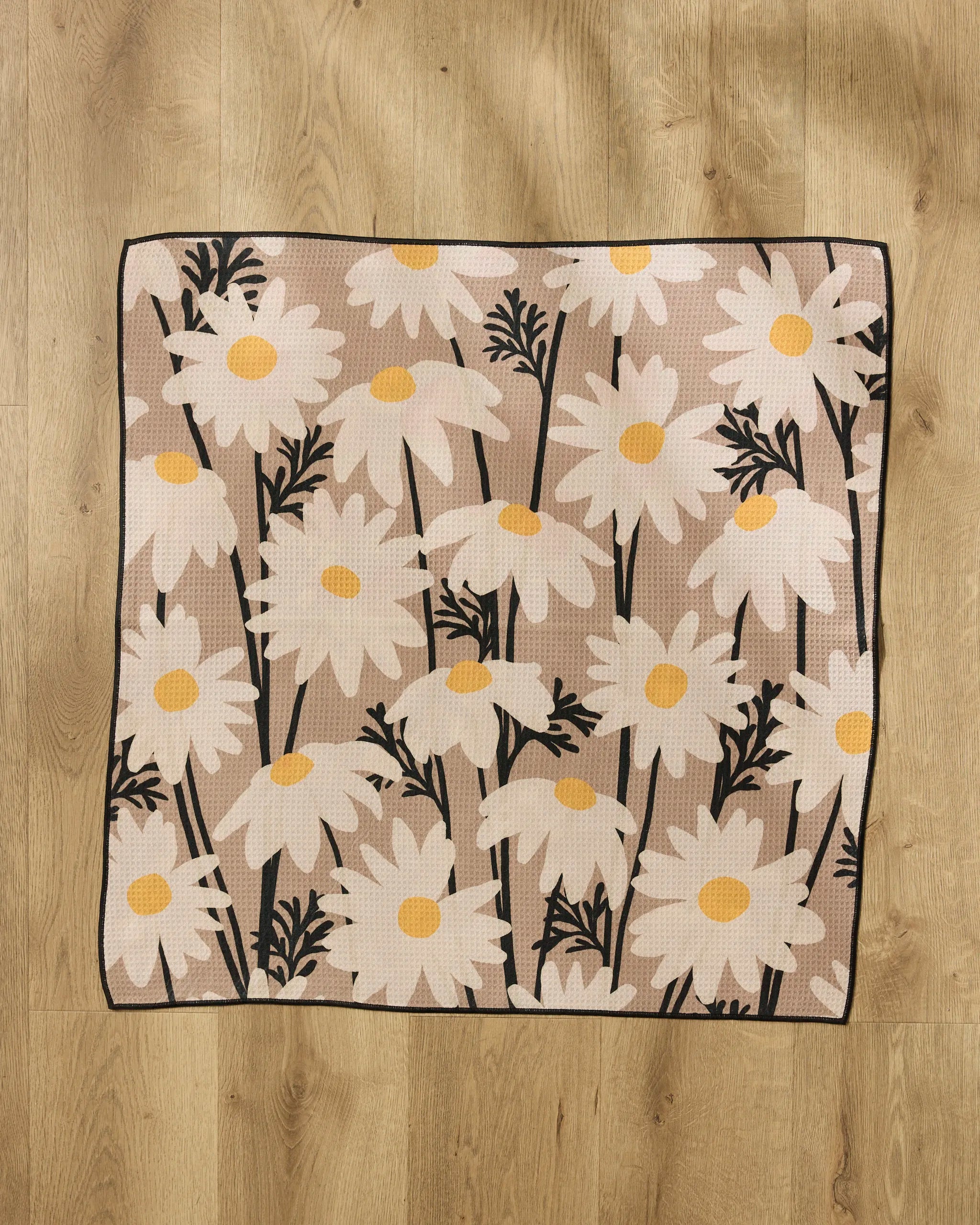 The "Sweet Daisies" rug by Geometry, made from recycled materials, has large white daisies with yellow centers and black stems and leaves, shown on a light wood floor.