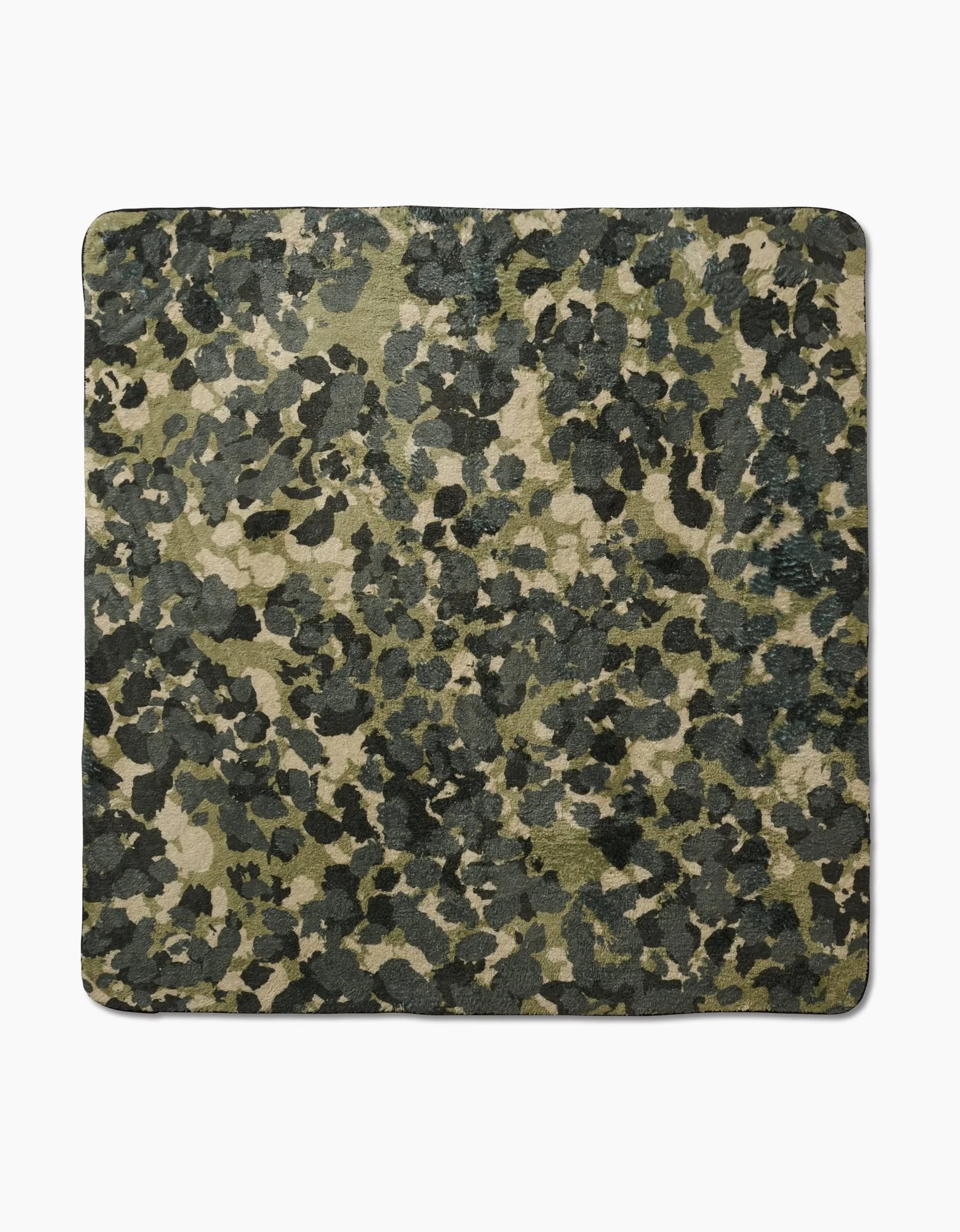 The Geometry Camo rug is a square design made from recycled materials, showcasing a green, black, and beige camouflage pattern on a white background.