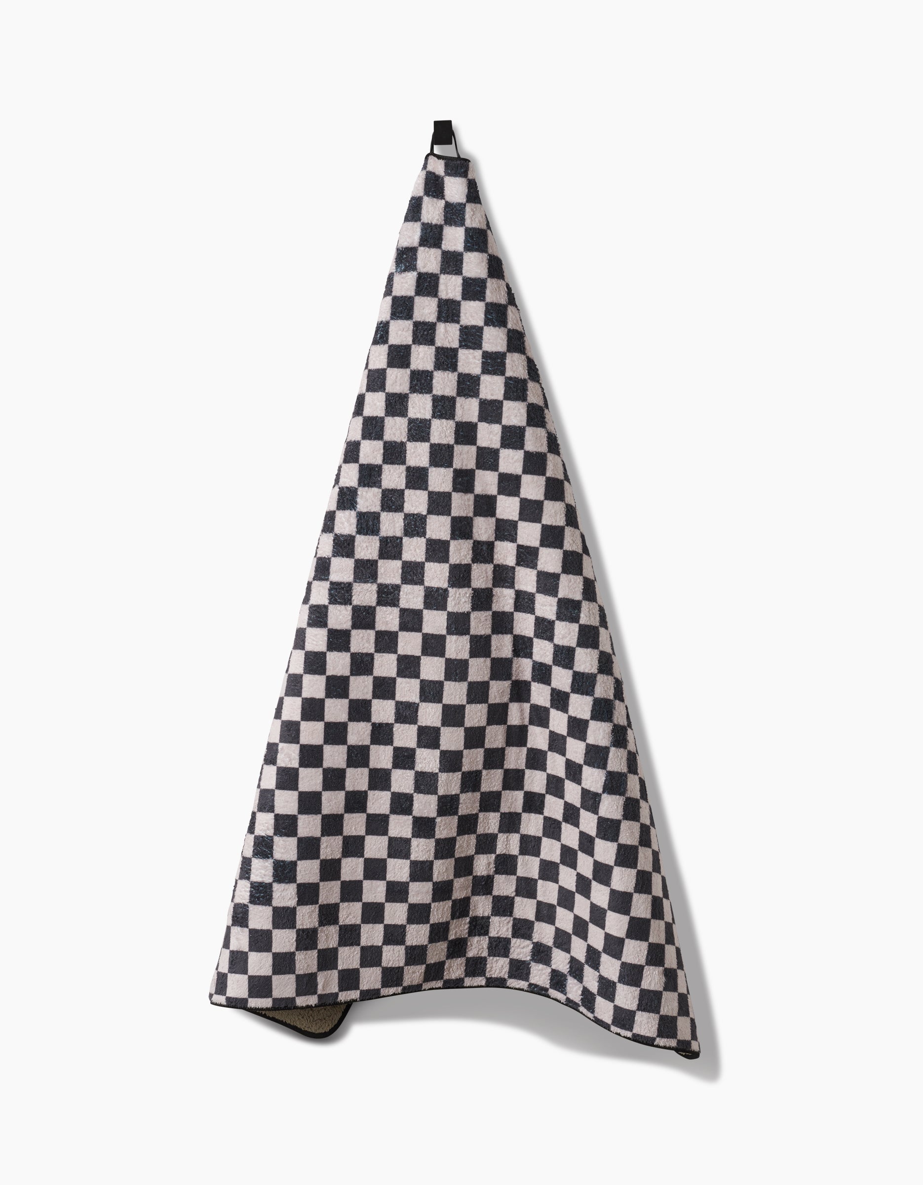 The Geometry Cool Pup is a plush dog towel with a black and white checkerboard pattern, made from recycled materials, shown hanging from a hook against a plain white background.