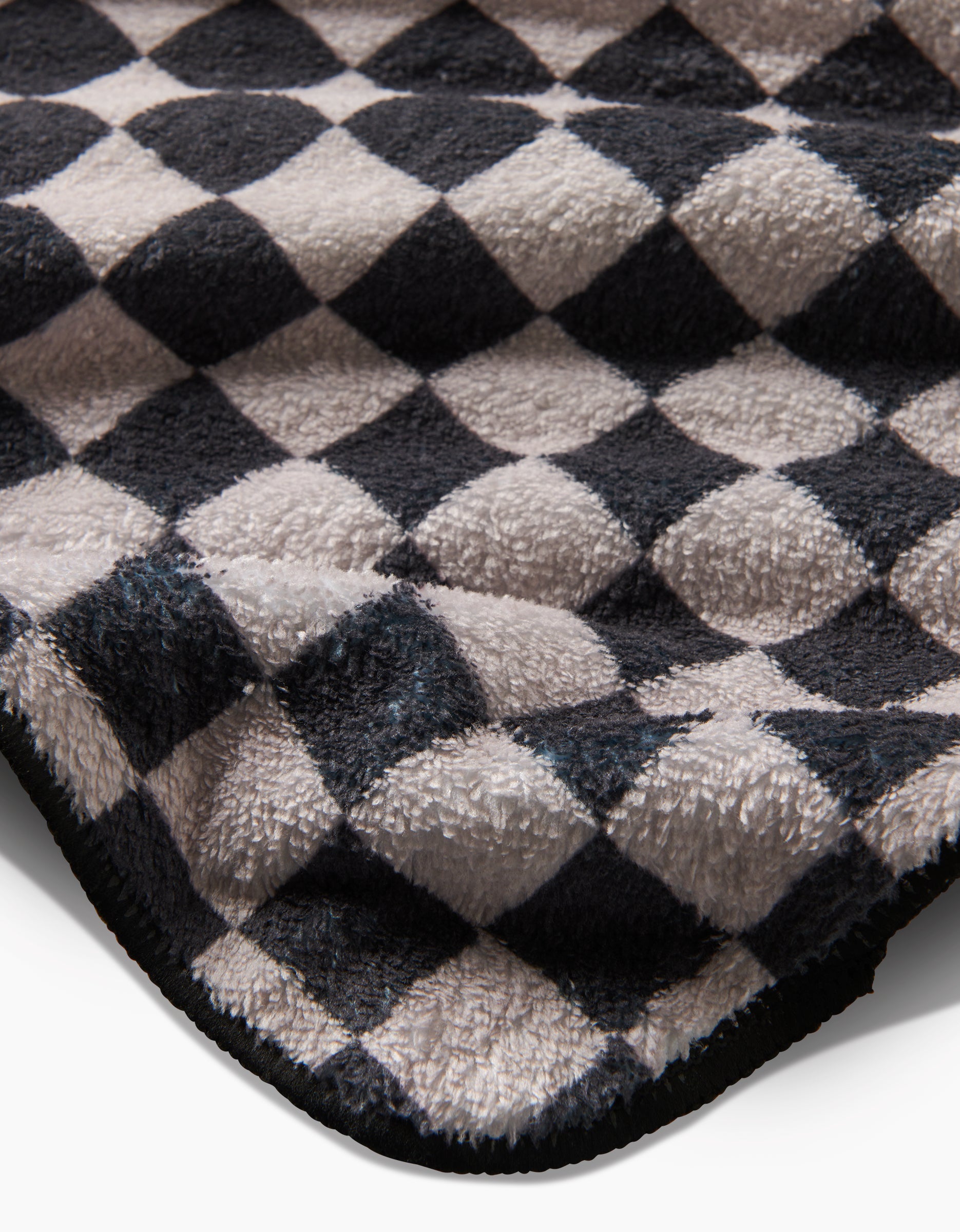 A close-up of the Geometry Cool Pup ultra-absorbent plush dog towel with a black and white checkered pattern, highlighting its textured surface and slightly curved edge.