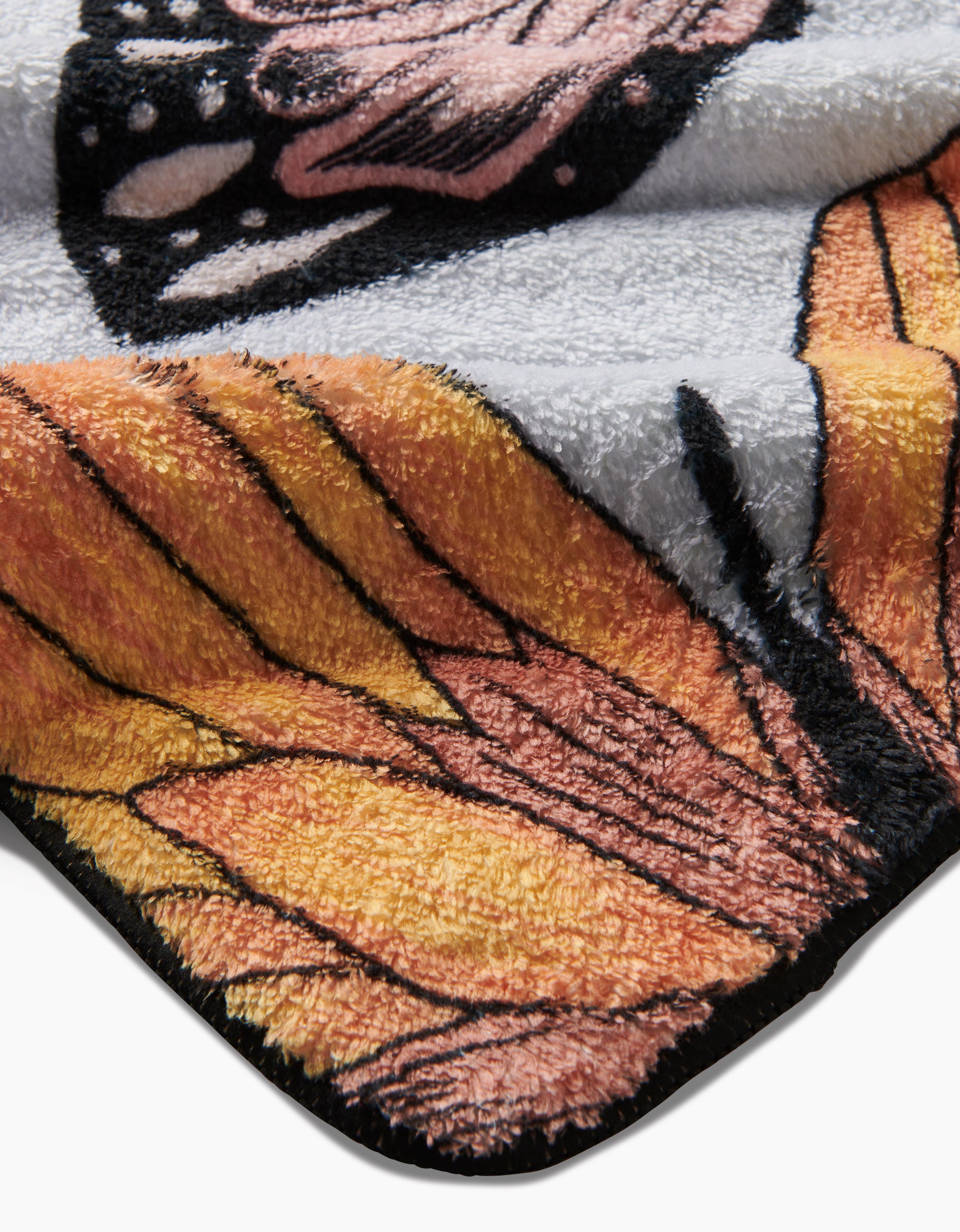 The Geometry Cute Butterflies blanket features a vibrant butterfly wing design in orange, yellow, black, and pink. Made from recycled materials, its ultra-absorbent velvety fabric is soft and plush with a neatly folded corner.