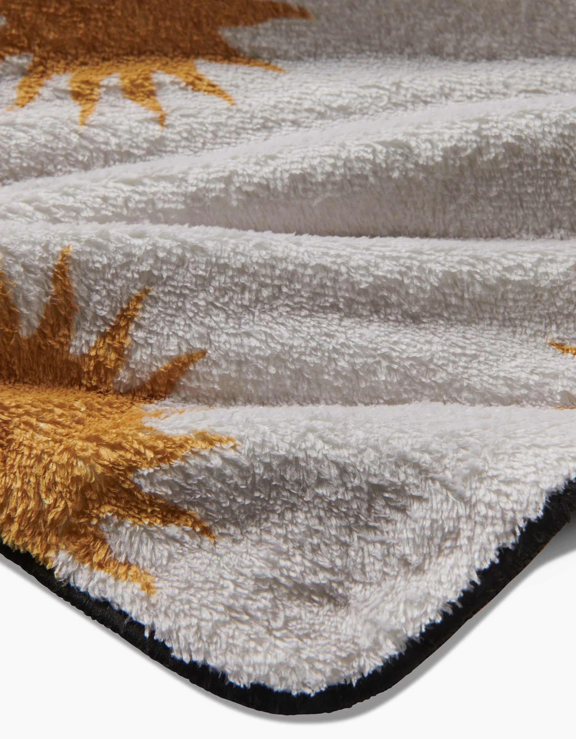 A close-up of Geometry’s Feeling Sunny plush dog towel, made from recycled materials with a soft white base, yellow sun designs, and a black border. The ultra-absorbent fabric lies in gentle folds.
