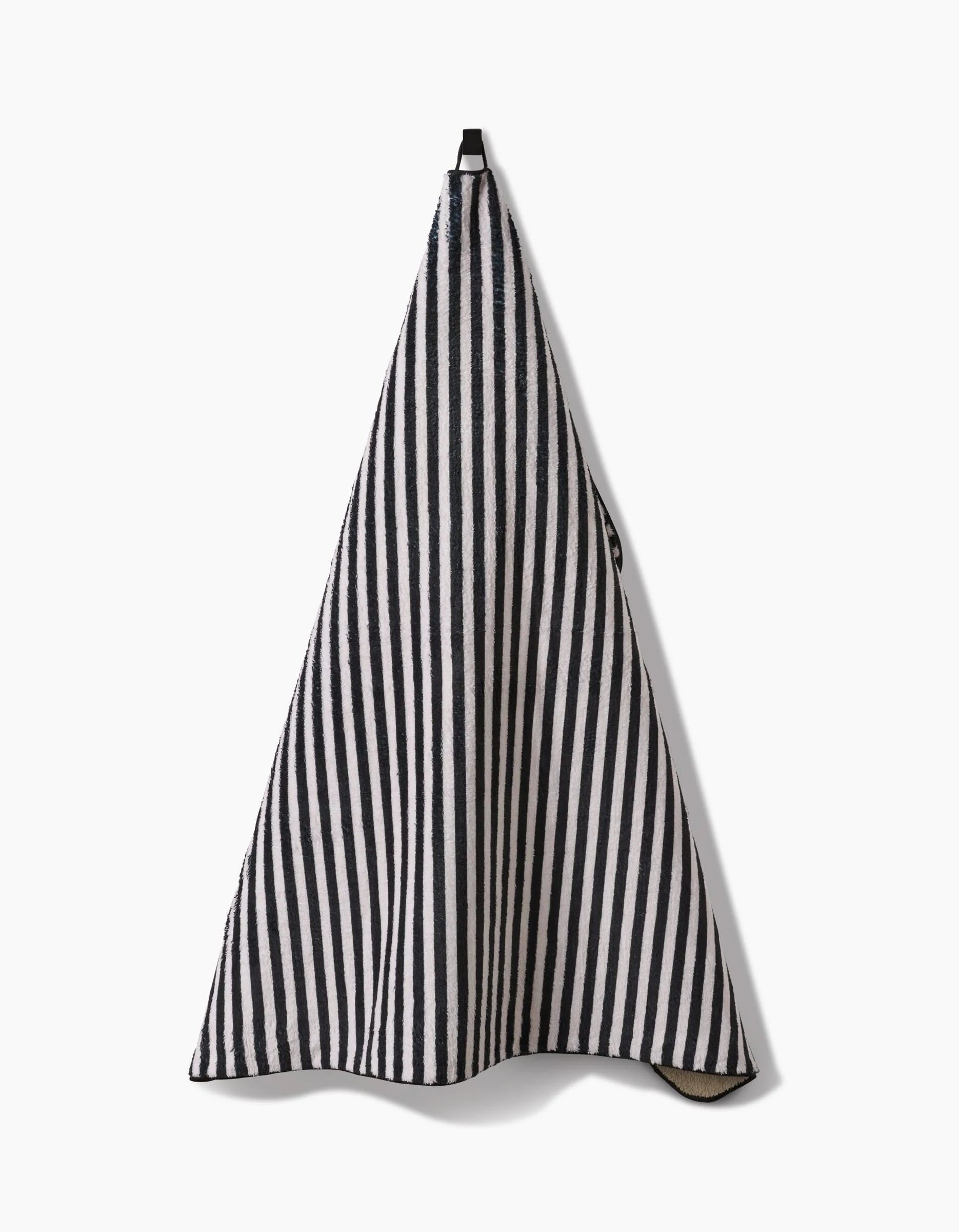 The Geometry Good Pup towel, featuring black and white vertical stripes, is ultra-absorbent and made from recycled materials. It hangs from a hook against a plain white background.