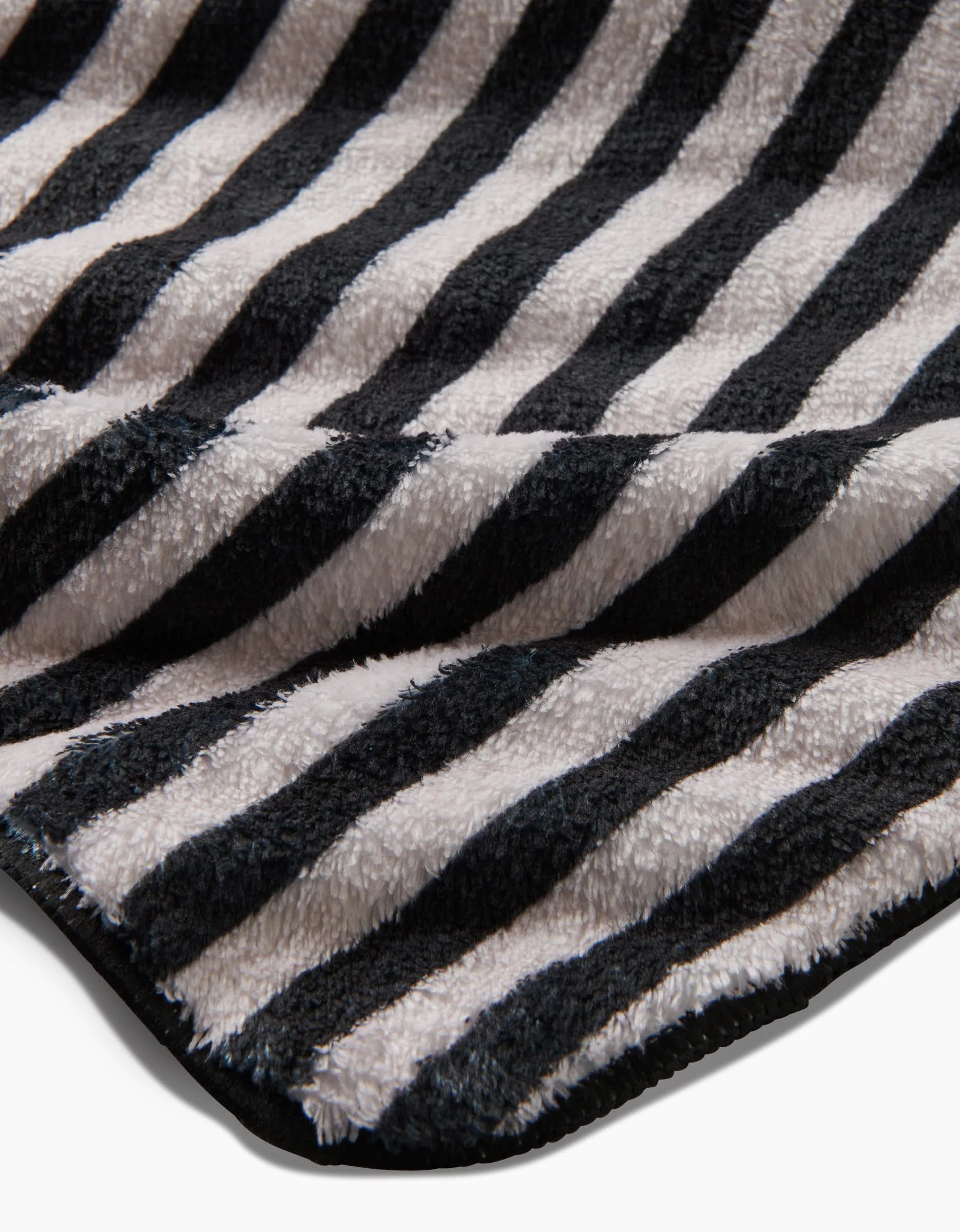 A close-up of Geometry’s Good Pup plush dog towel, featuring ultra-absorbent fabric with black and white horizontal stripes and a black-trimmed edge.
