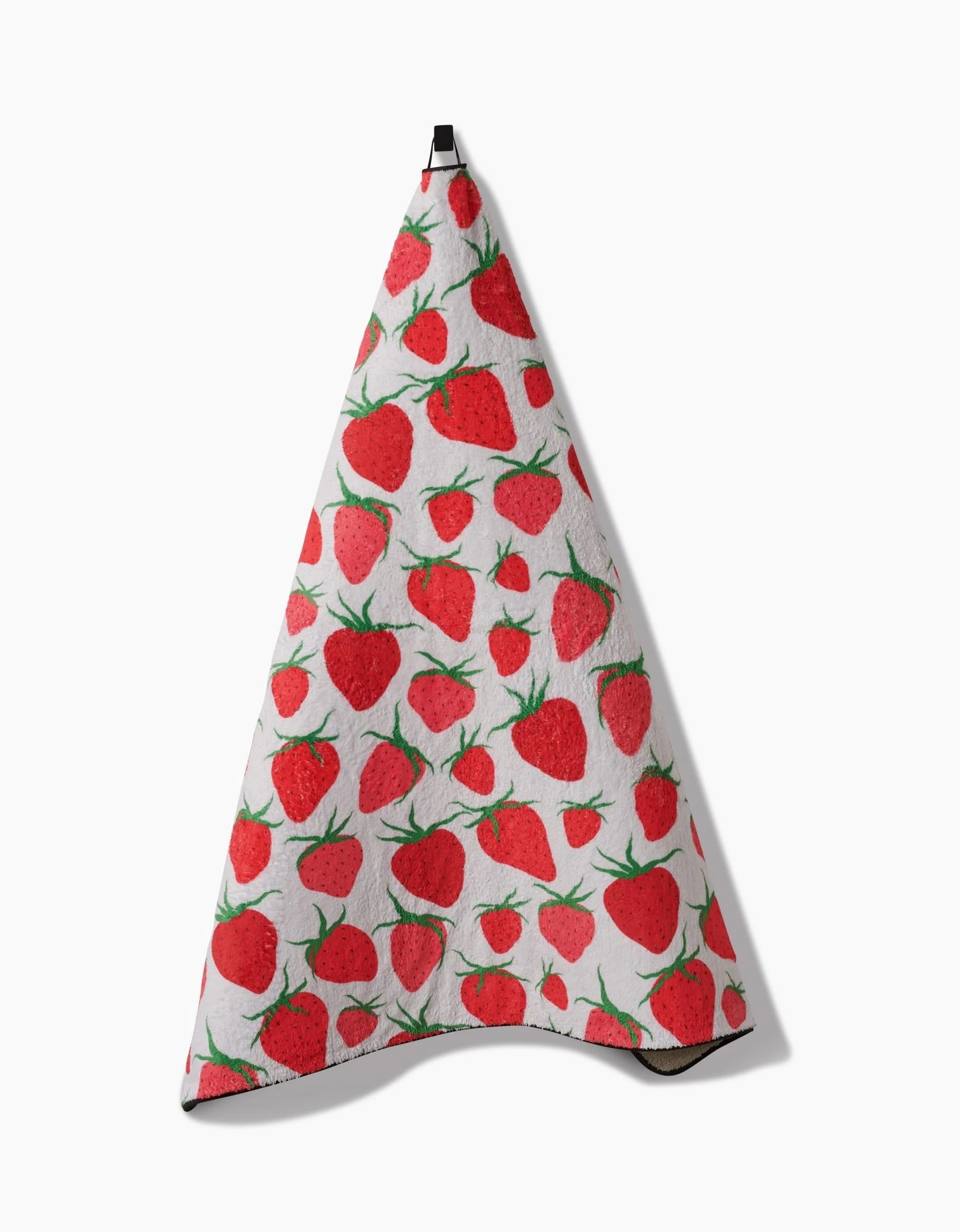 The Geometry Strawberry Sniff towel, featuring vibrant red strawberries and green leaves, hangs from a black loop against a plain white background.