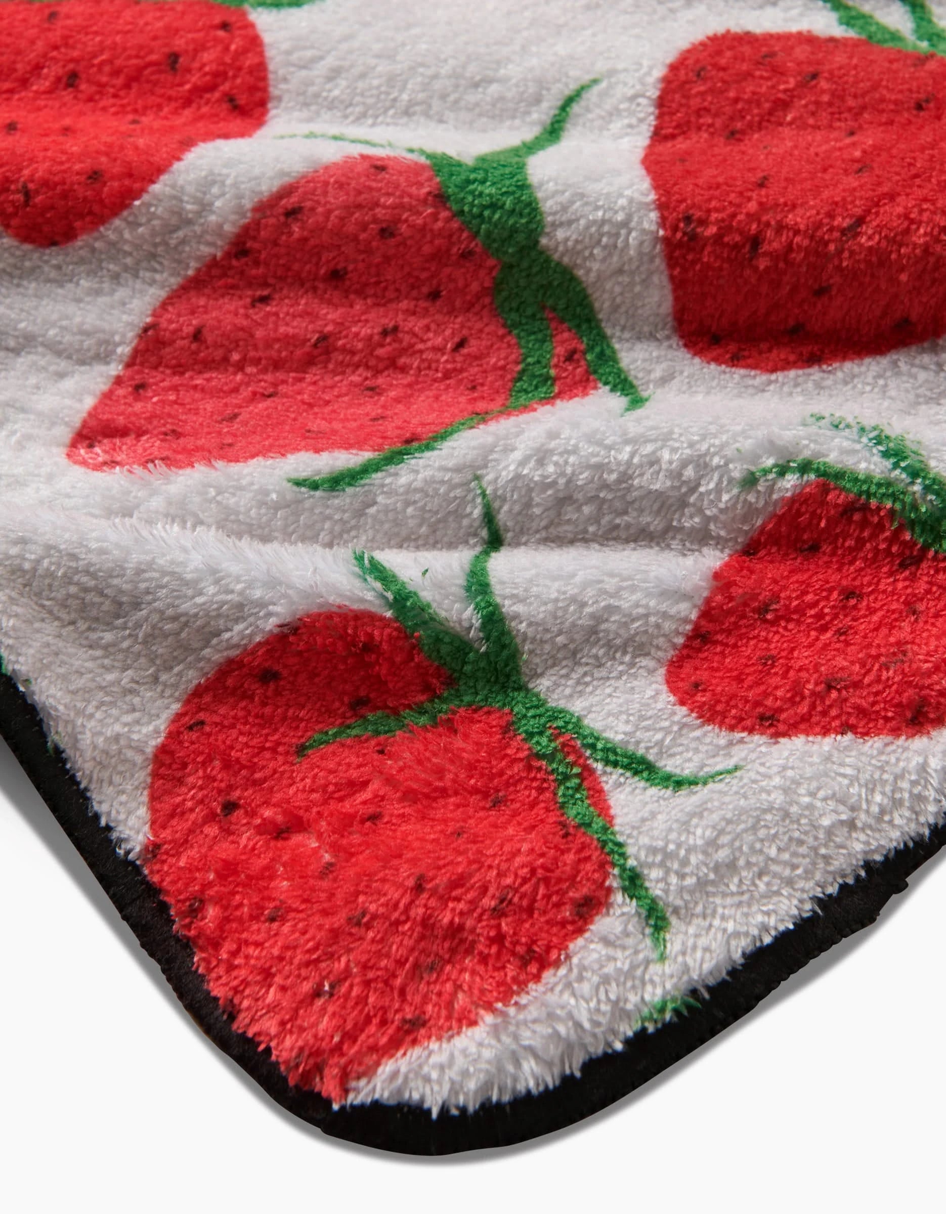 A close-up of the Geometry Strawberry Sniff towel, an ultra-absorbent white plush dog towel featuring a red strawberry pattern with green leaves. The fluffy towel is slightly folded, highlighting its soft texture and colorful design.