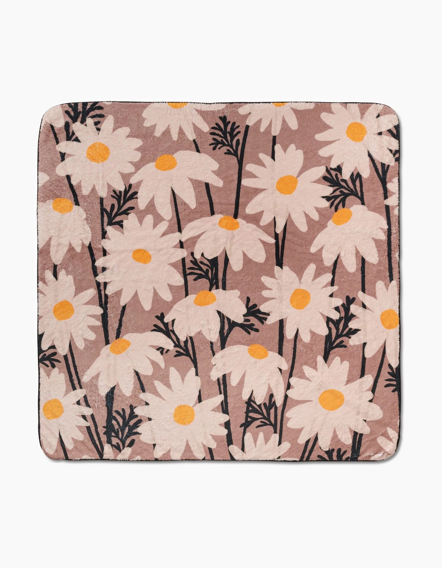 The Geometry Sweet Daisies blanket is a square, eco-friendly throw featuring large white daisies with yellow centers and black stems on a light brown background.