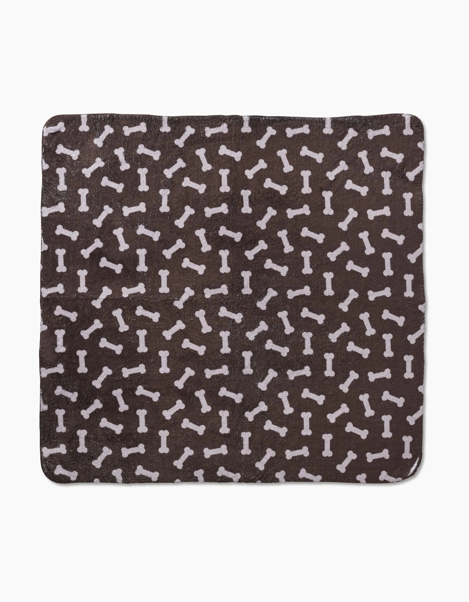 Geometry’s “Sweet Treats” is a square, dark brown plush dog towel with a white dog bone pattern, made from ultra-absorbent recycled materials.