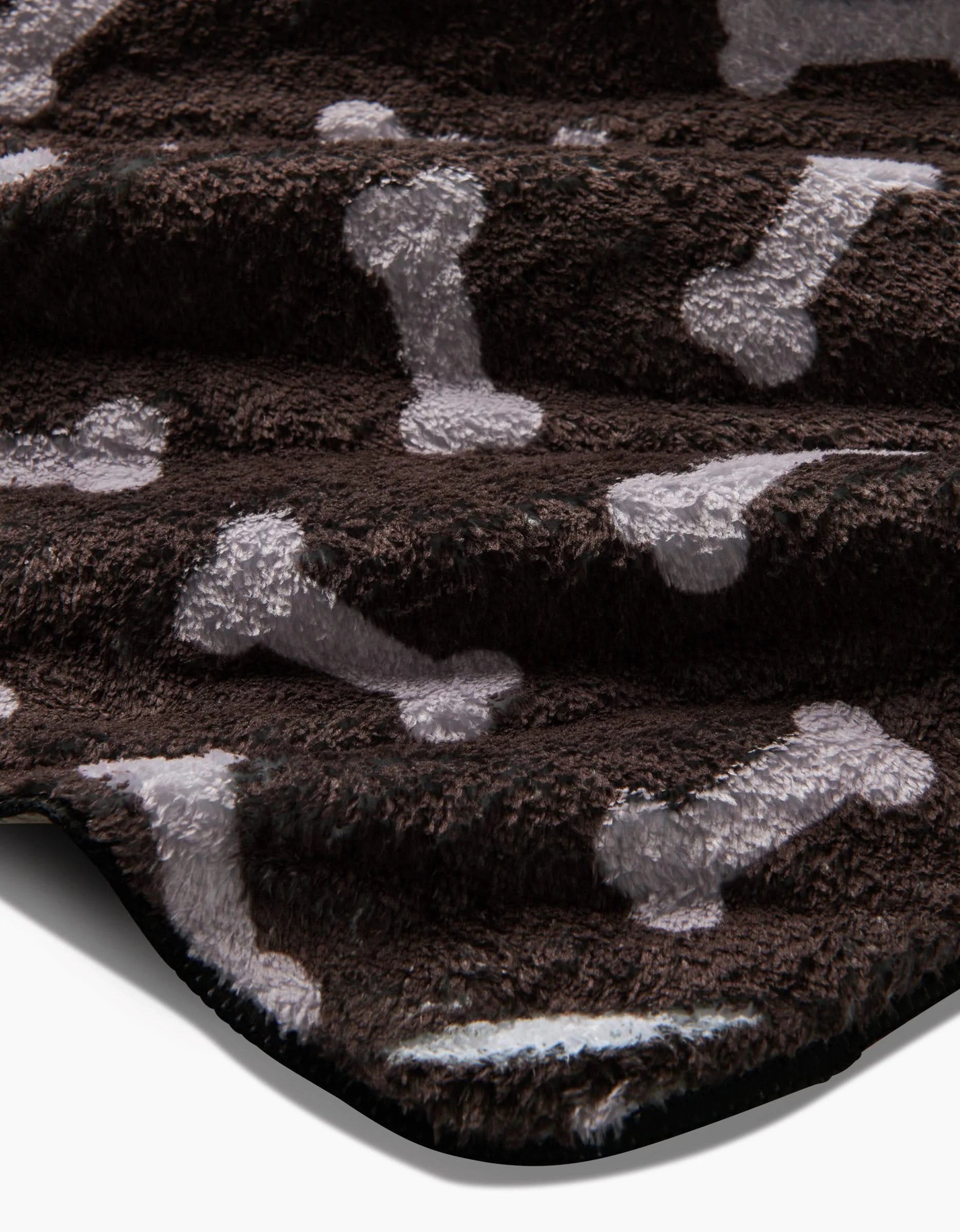 Close-up of the Sweet Treats plush dog towel by Geometry, crafted from recycled materials with a soft, dark brown surface adorned with light gray dog bones.