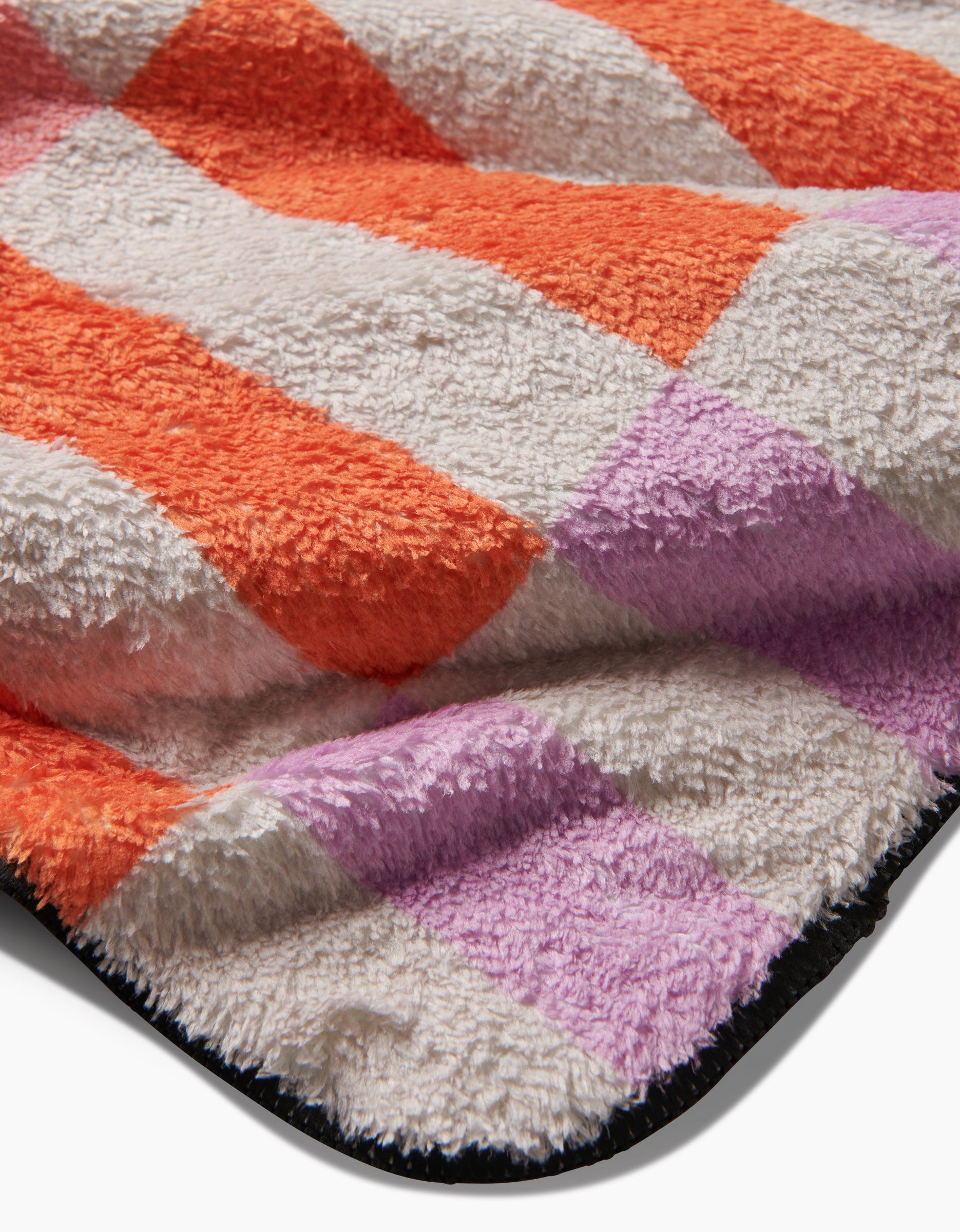 The Wag Wise blanket by Geometry is soft and fuzzy, made from recycled materials, and features an orange, lavender, and off-white checkered pattern with a black trimmed edge.