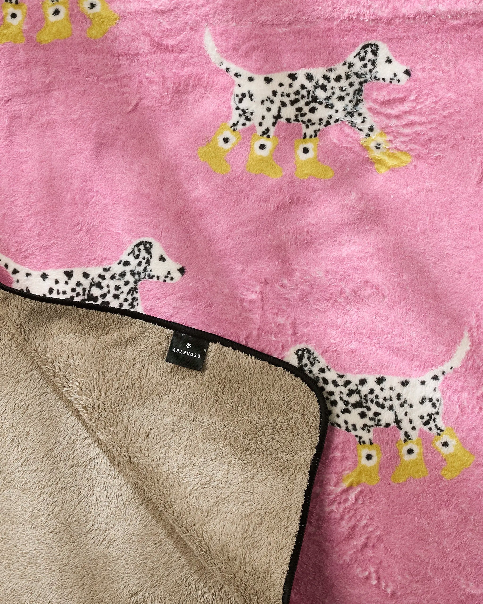 The Geometry Dalmatian In Boots Pink towel features illustrated Dalmatians in yellow boots on a pink background. Soft, ultra-absorbent, and partially folded to show its beige underside, it's a cute and practical choice for your dog.