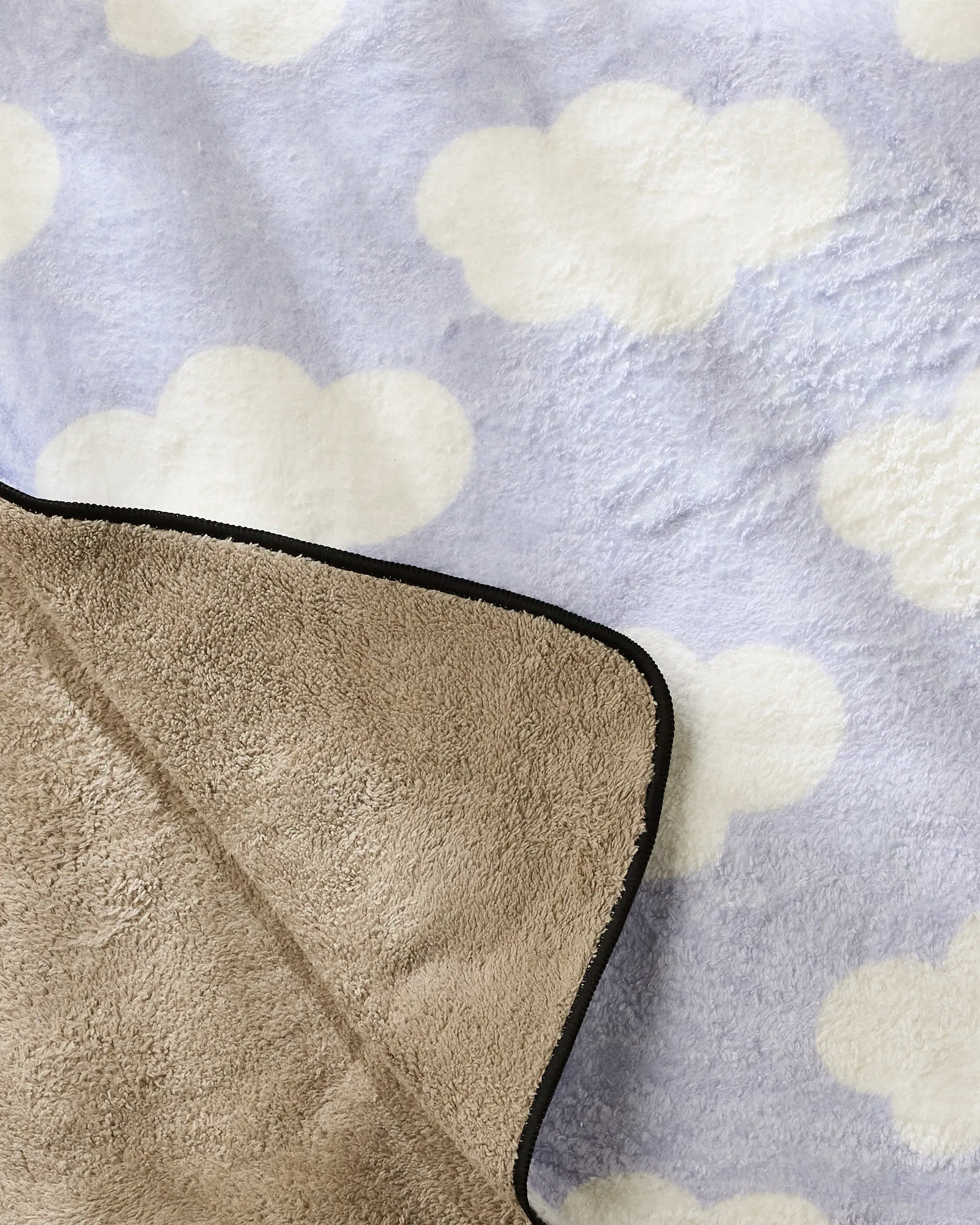 Letters By Shells’ Dreamy Clouds is a soft, plush dog towel featuring a light blue background with white clouds, partially folded to show its plain beige underside and black-trimmed edges.