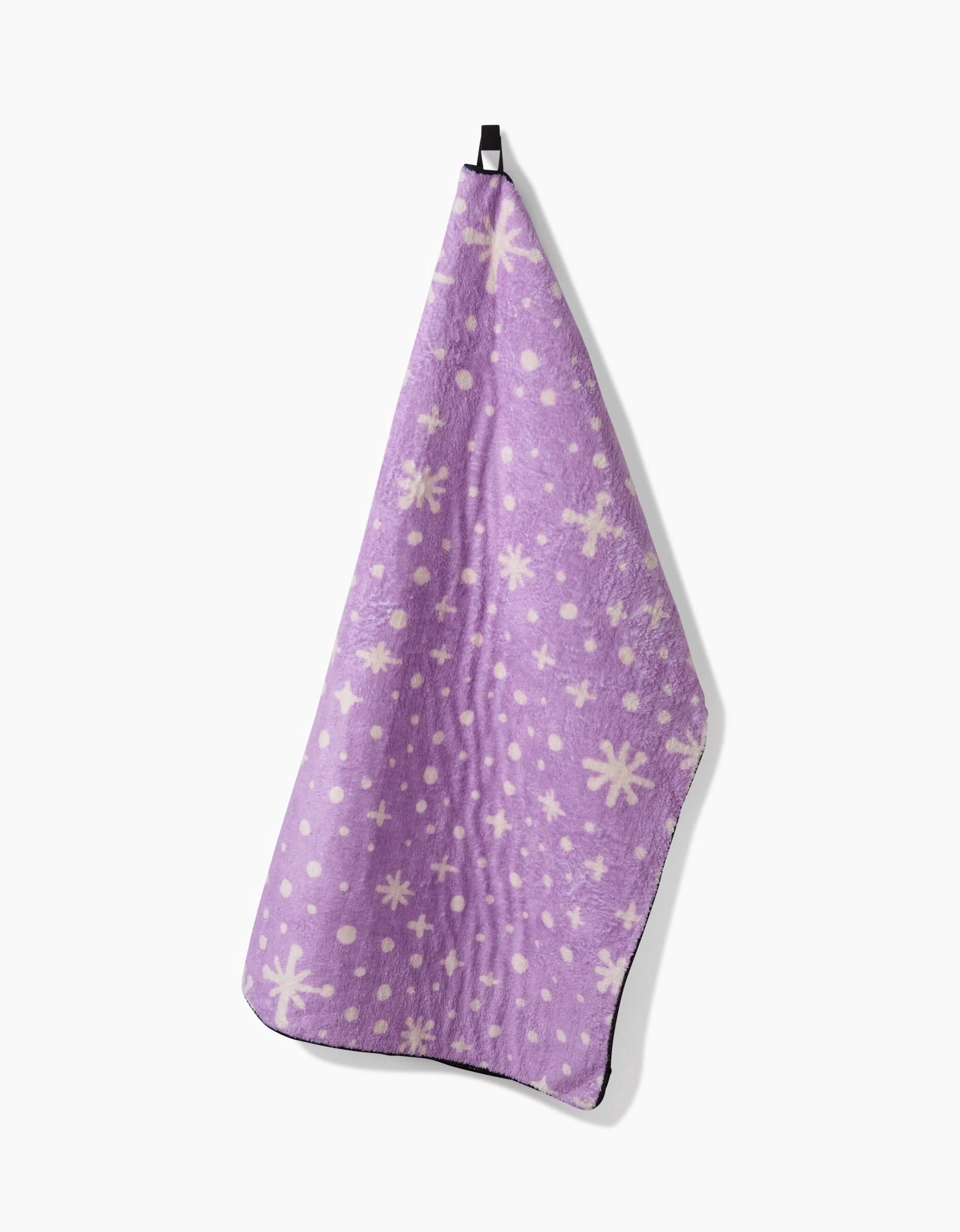 The Amy MacCready Estrella Purple dog towel, featuring white star and dot patterns, hangs on a black hook against a plain white background.