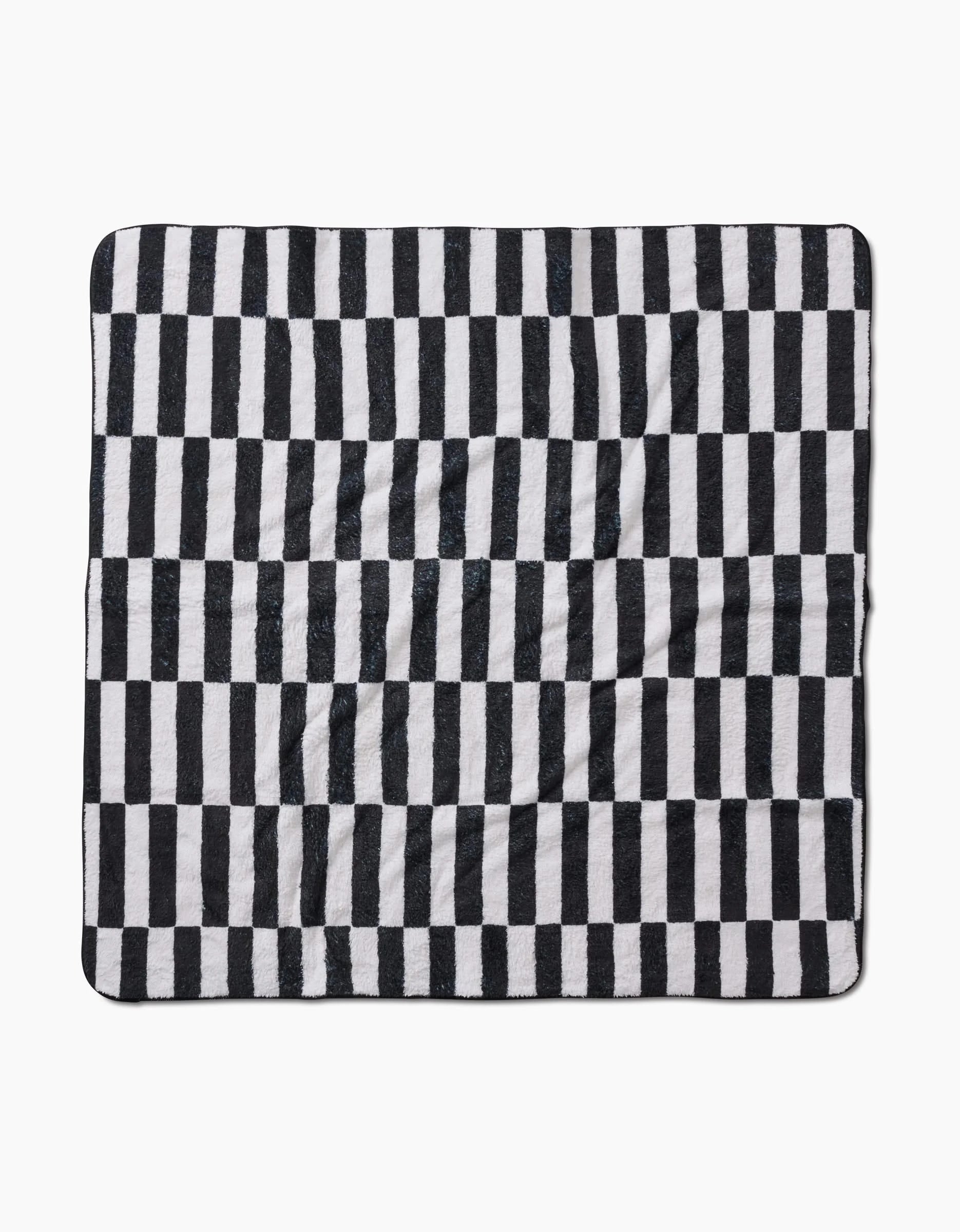The Hufton Studio Long Check is a square blanket made from recycled materials, with a black and white vertical check pattern. Its ultra-absorbent fabric looks soft and slightly wrinkled, shown flat against a white background.