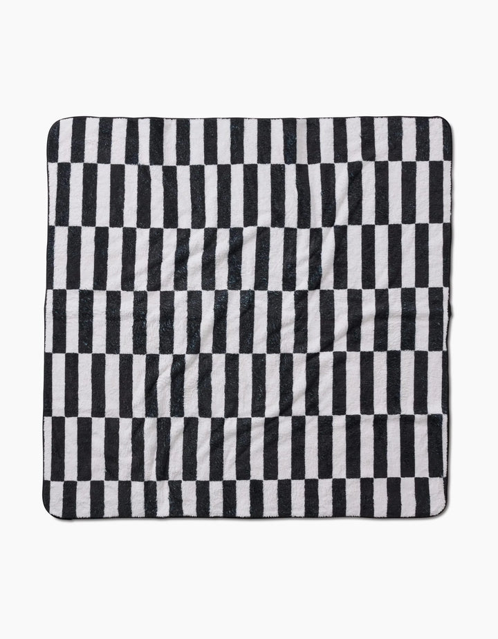 The Hufton Studio Long Check is a square blanket made from recycled materials, with a black and white vertical check pattern. Its ultra-absorbent fabric looks soft and slightly wrinkled, shown flat against a white background.
