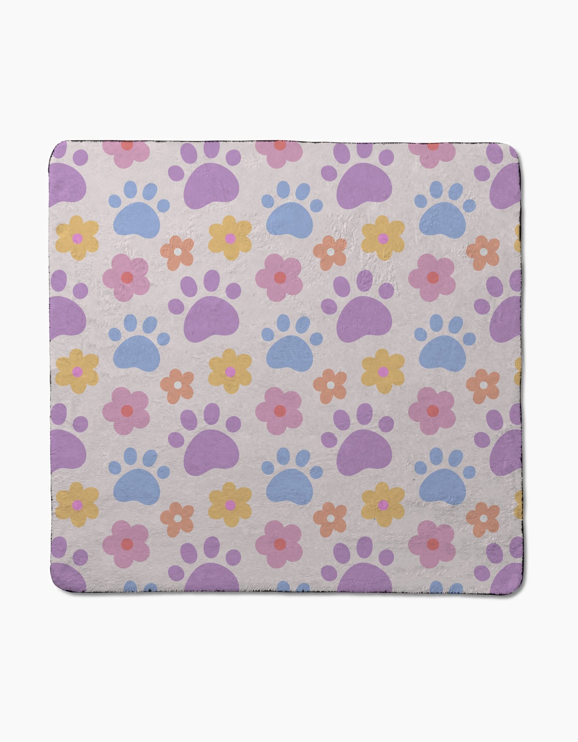 The Paws and Daisies dog towel by Letters By Shells showcases a pastel print of purple and blue paw prints with pink, yellow, and orange flowers on a light beige background.