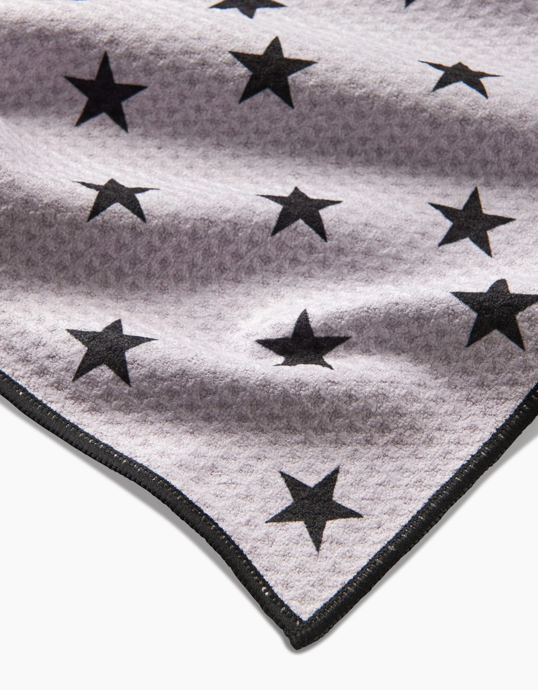A close-up of Geometrys Bark Paw Towel, made from ultra-absorbent Geoweave fabric in light gray with black stars and a stitched black edge.