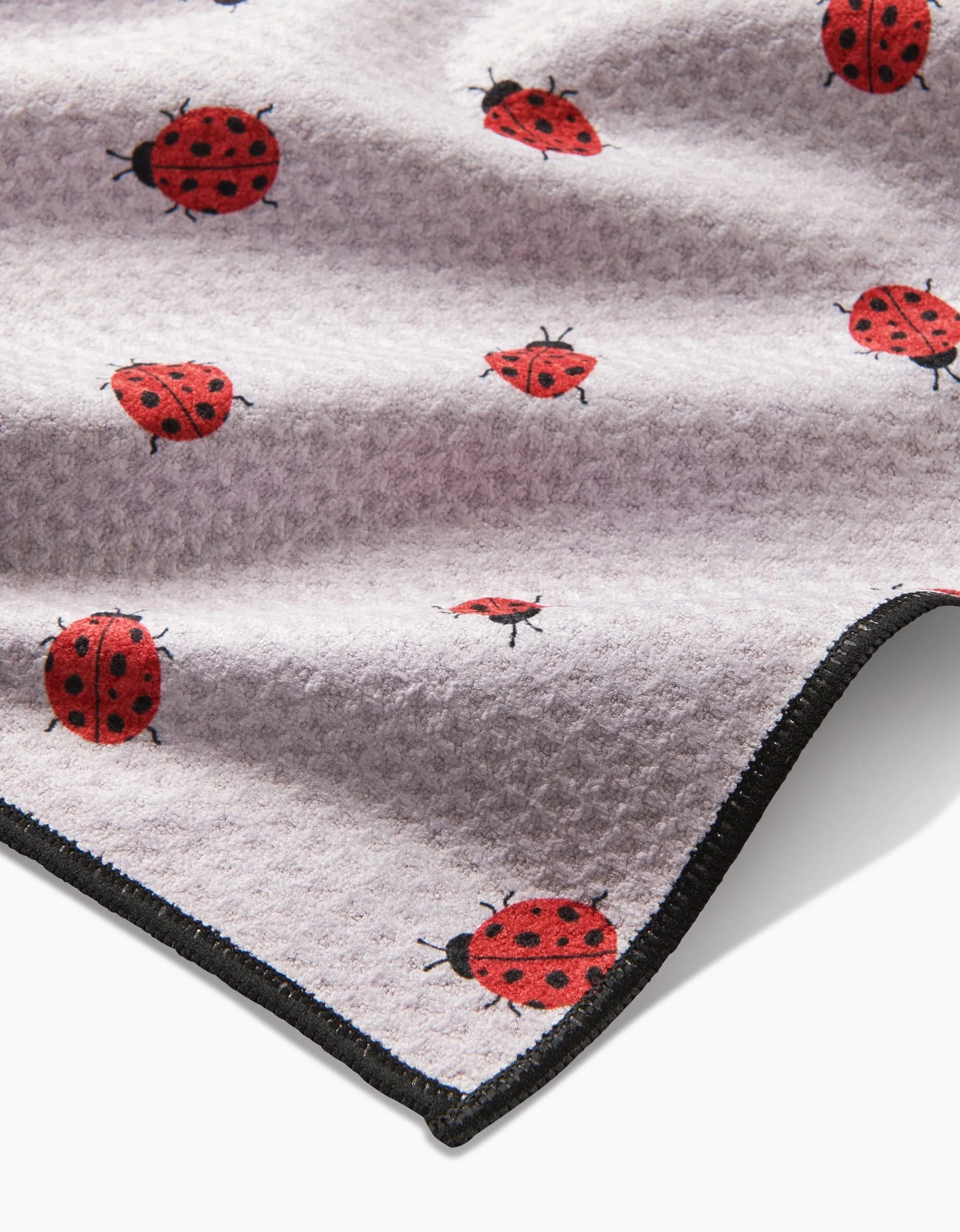 A close-up of the ultra-absorbent white Geoweave fabric on Geometry’s Bugsy towel, featuring a red and black ladybug pattern and a sleek black-trimmed edge.