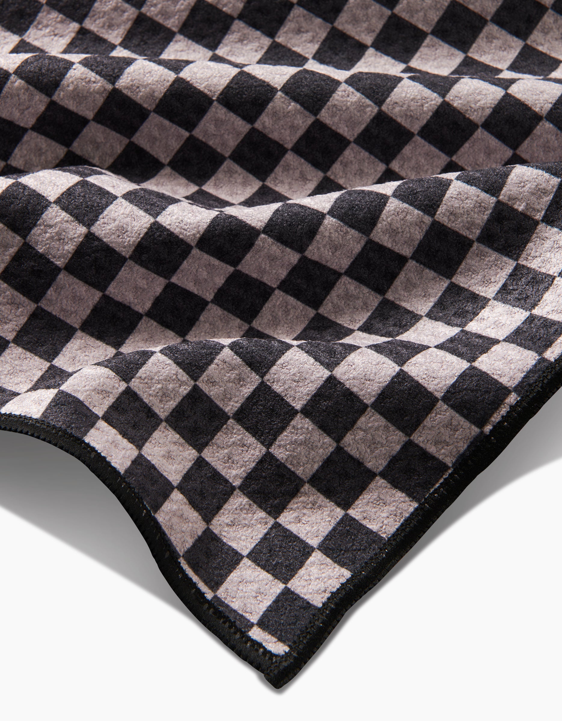 A close-up of Cool Pup by Geometry, featuring soft Geoweave fabric with a black and beige checkerboard pattern. Slightly folded at the edges, this ultra-absorbent towel is perfect for drying your pets paws.