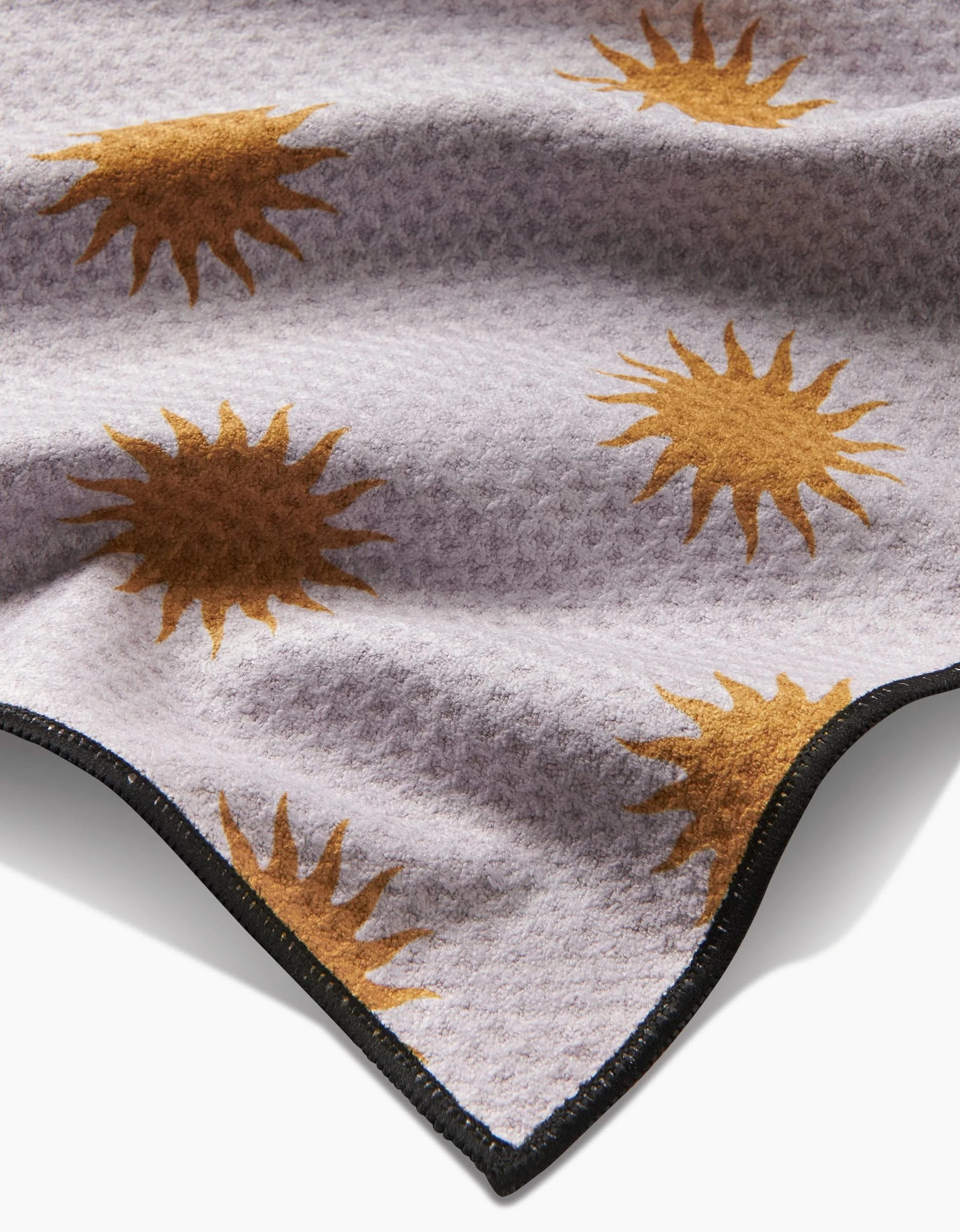 A close-up of Geometrys Feeling Sunny blanket, featuring textured light gray Geoweave fabric with golden yellow sunburst patterns and a black-trimmed edge.