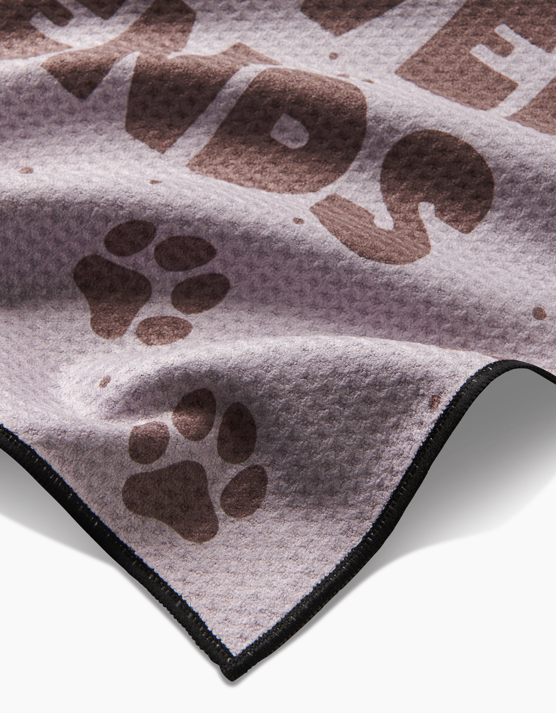 A close-up of the Geometry Fur Ever Friends Paw Towel shows its light purple Geoweave fabric with brown paw prints, bold FRIENDS text, and a sleek black border for ultra-absorbency.