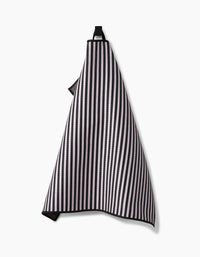 The Geometry Good Pup kitchen towel, featuring black and white vertical stripes and made from recycled materials, hangs on a hook against a plain white background.