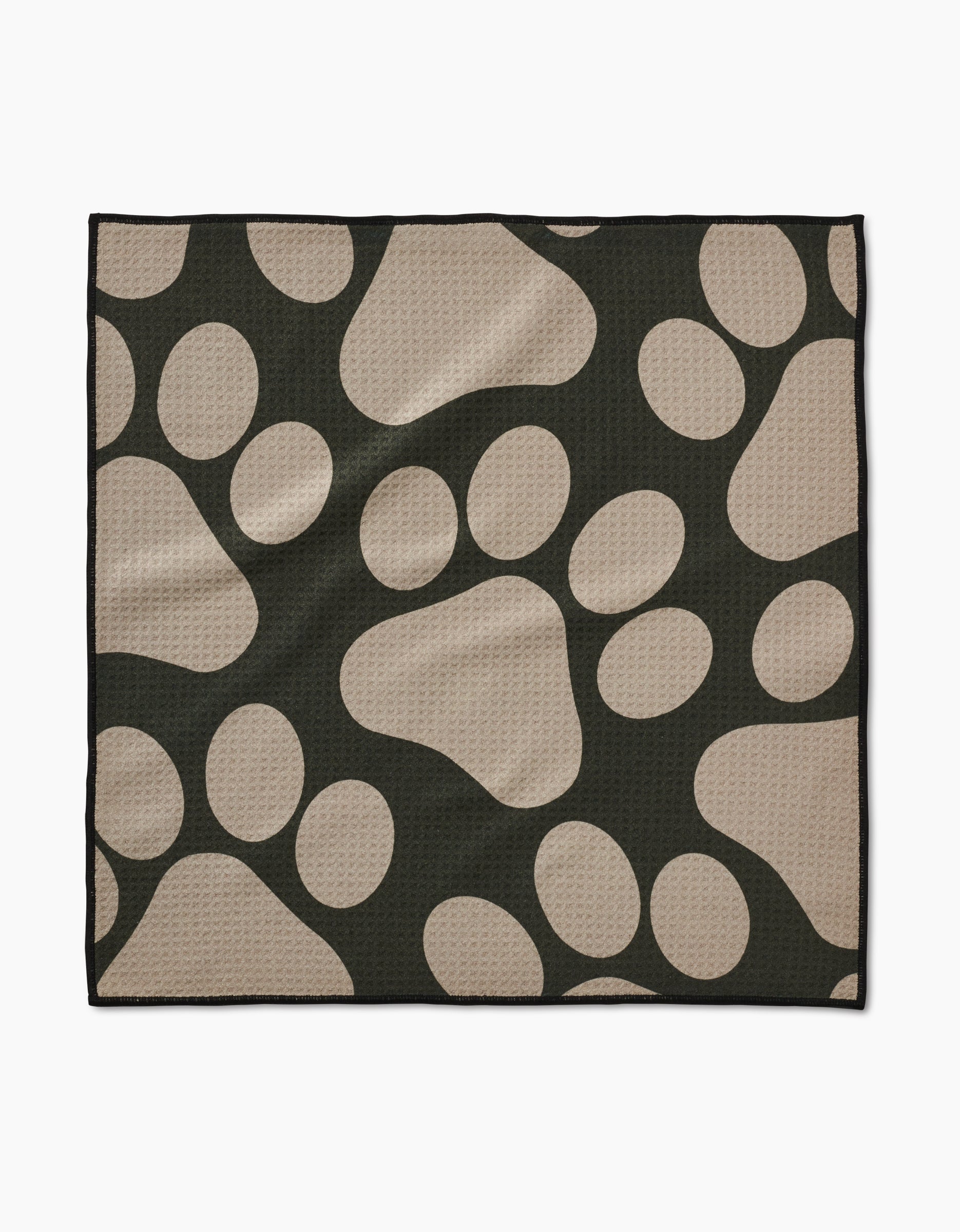 The Geometry Paw Prints mat is a black, rectangular towel with large tan paw prints on its ultra-absorbent, textured surface. Made from recycled materials, it has a clean black border for a simple finish.